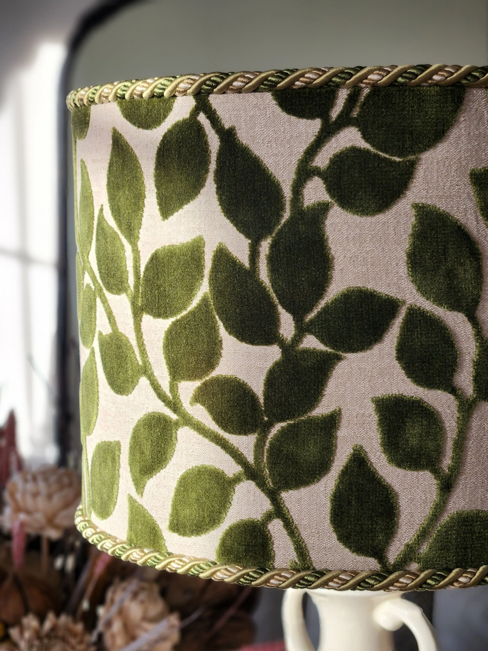 Close-up of a lampshade with a green leaf pattern and rope trim at the top and bottom edges.