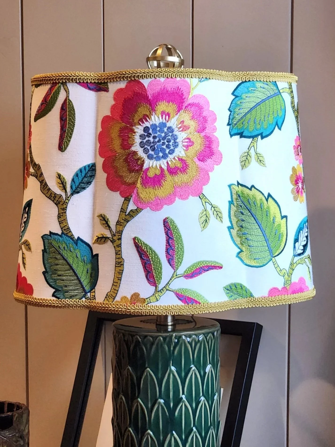 A decorative table lamp with a floral-themed lampshade featuring colorful flowers and leaves, and a green lamp base.
