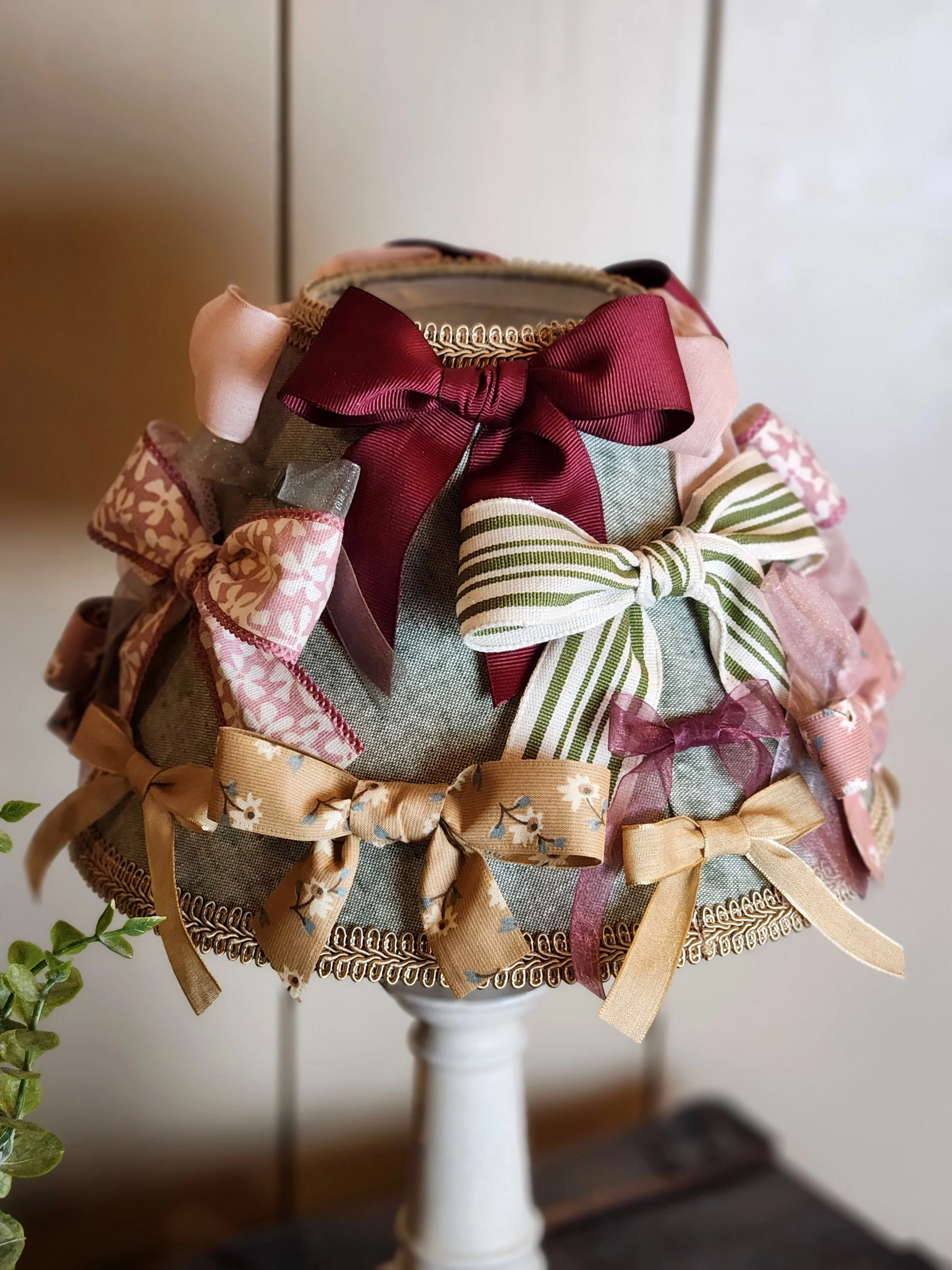 A decorative container with colorful bows made of various patterned ribbons, placed on a white stand against a plain background.