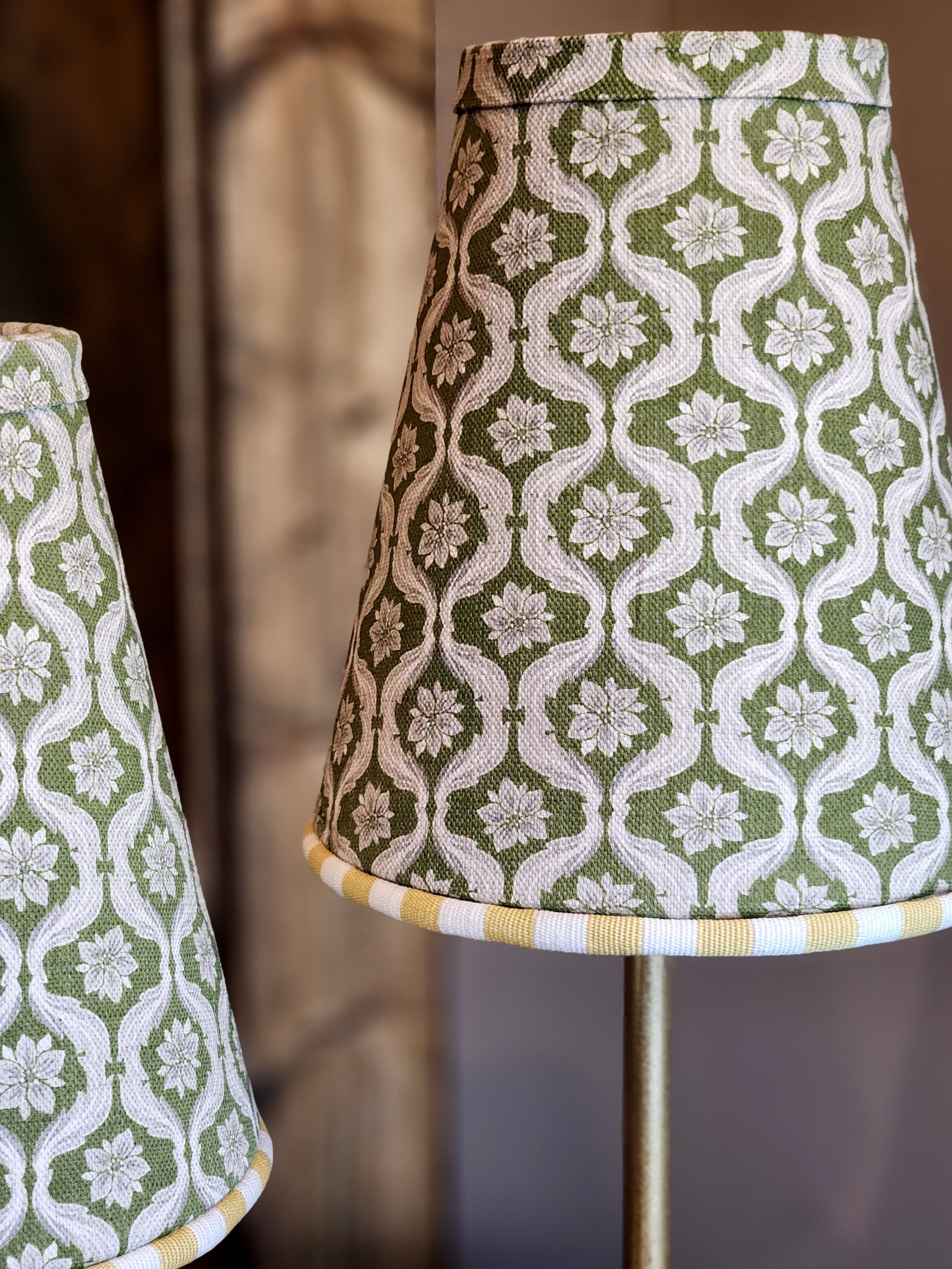 Close-up of a fabric lampshade with a green and white floral and vine pattern.