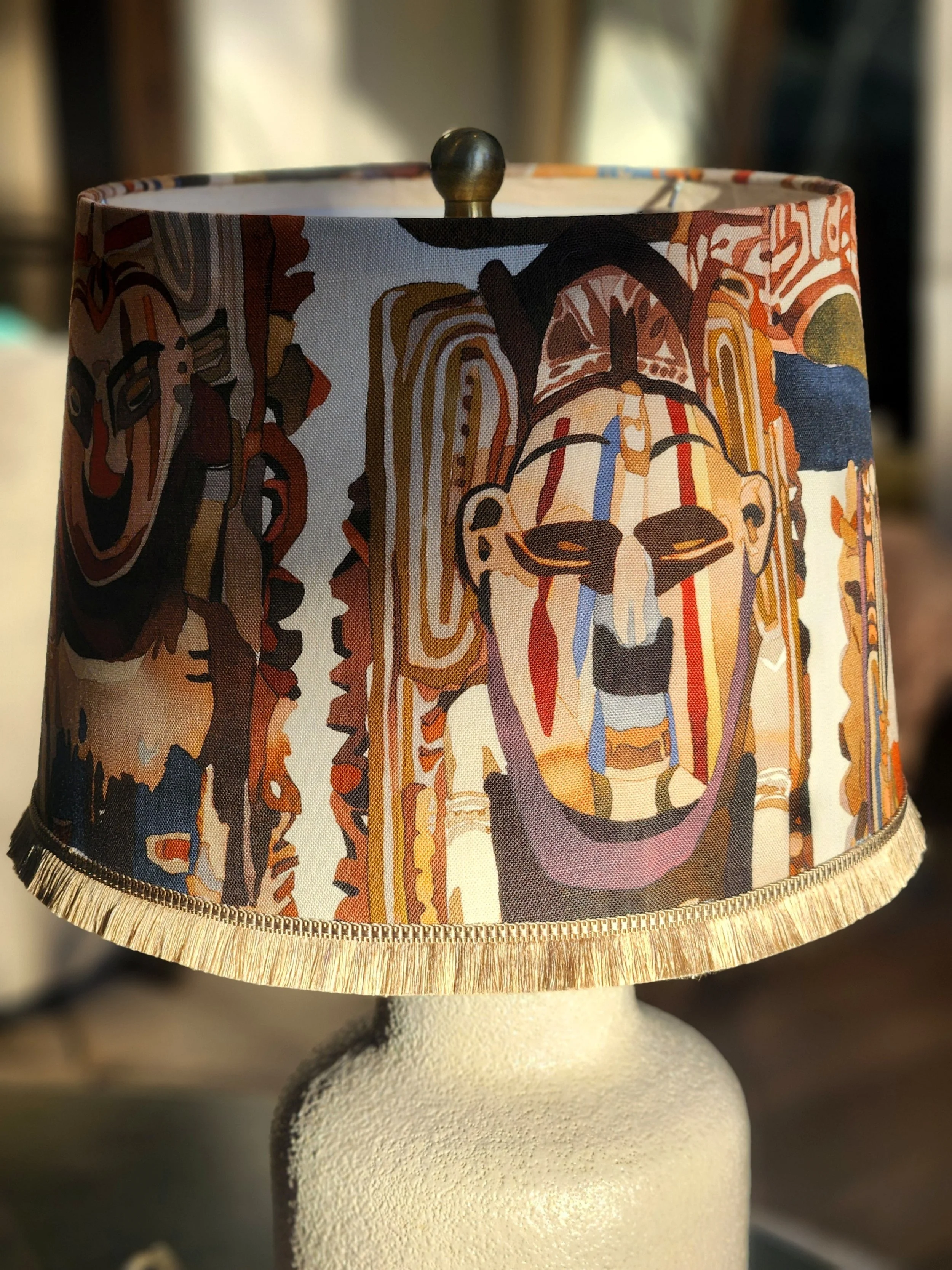 Lampshade with colorful, abstract artwork of a human face with tribal mask features.