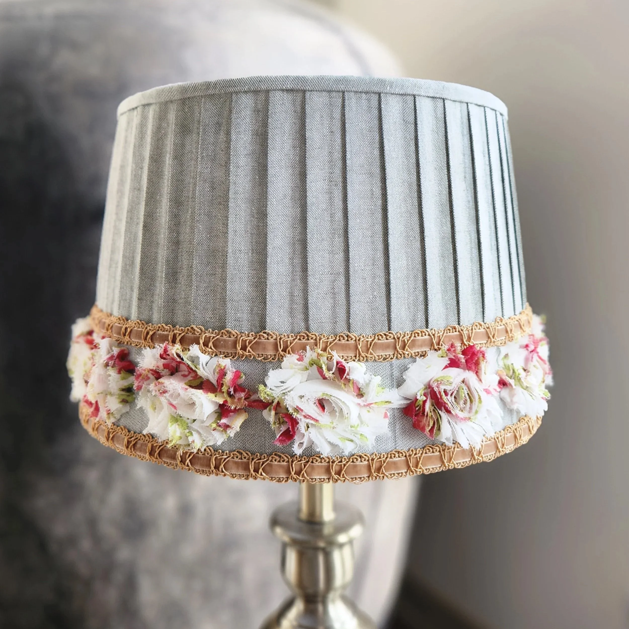 A lampshade with a gray fabric exterior and a floral trim around the bottom edge.