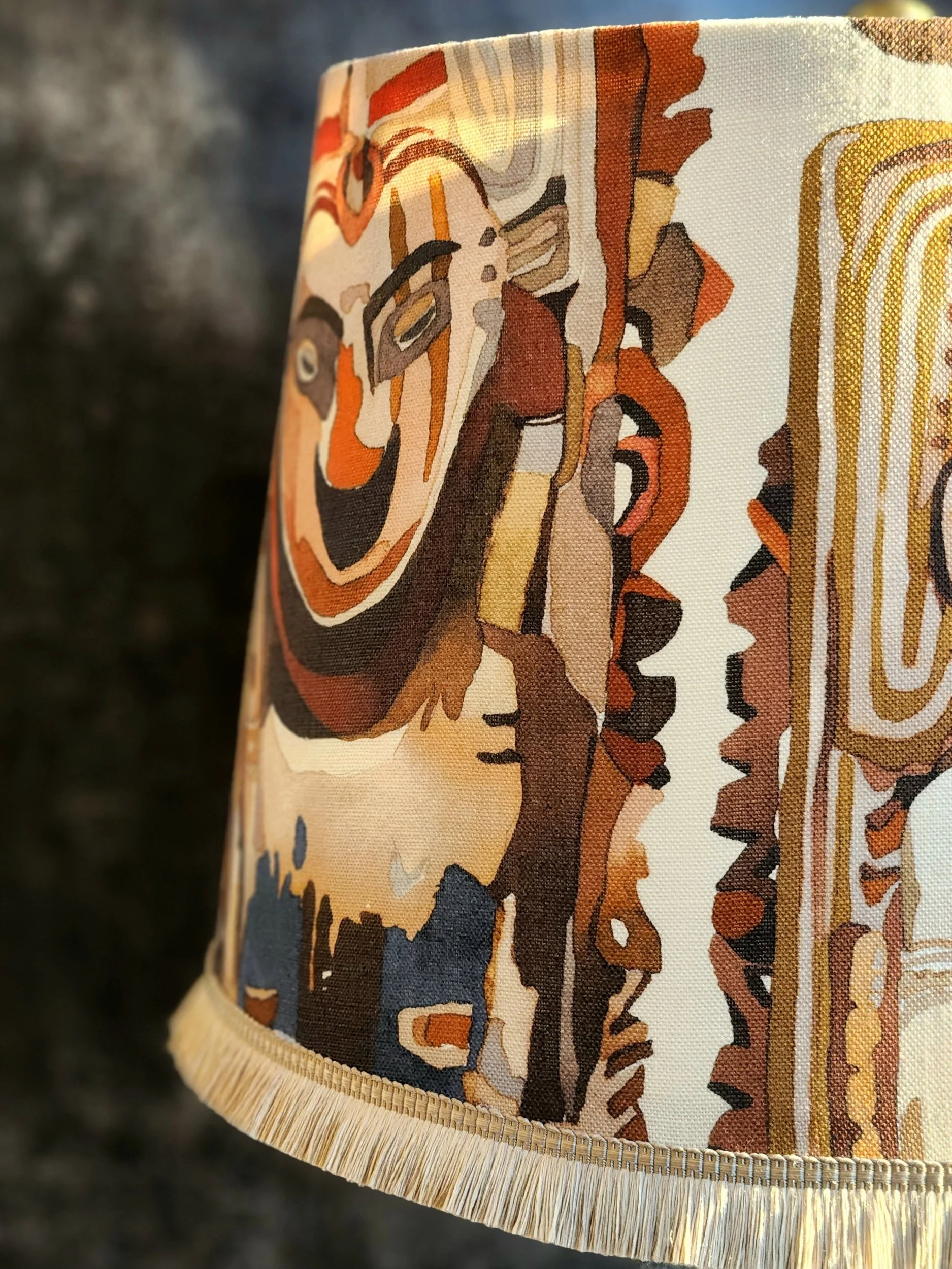 Close-up of a lampshade with an abstract painting design in earth tones, featuring swirling patterns and geometric shapes.