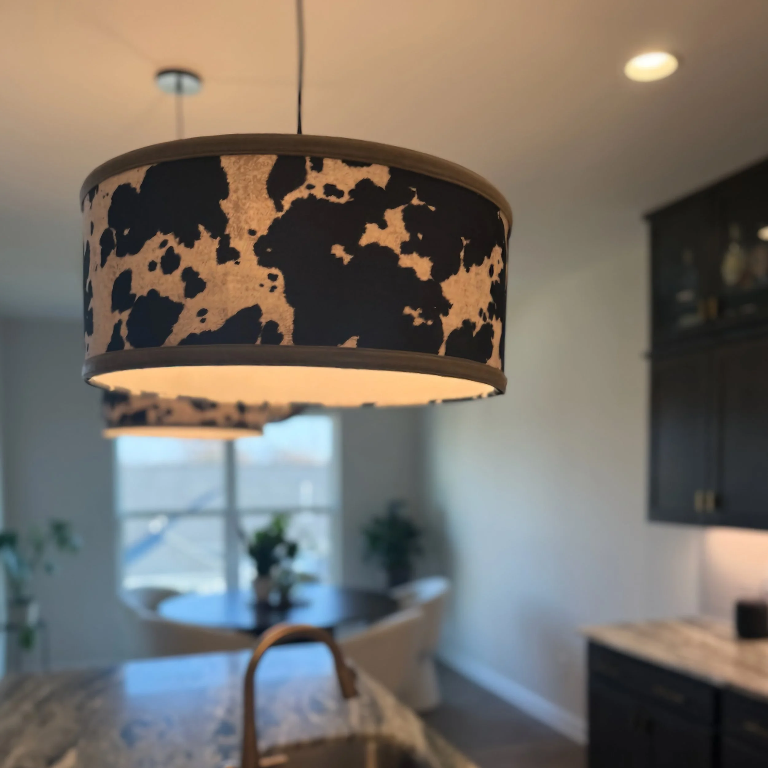 Close-up of a cowhide-patterned lampshade hanging over a kitchen countertop.