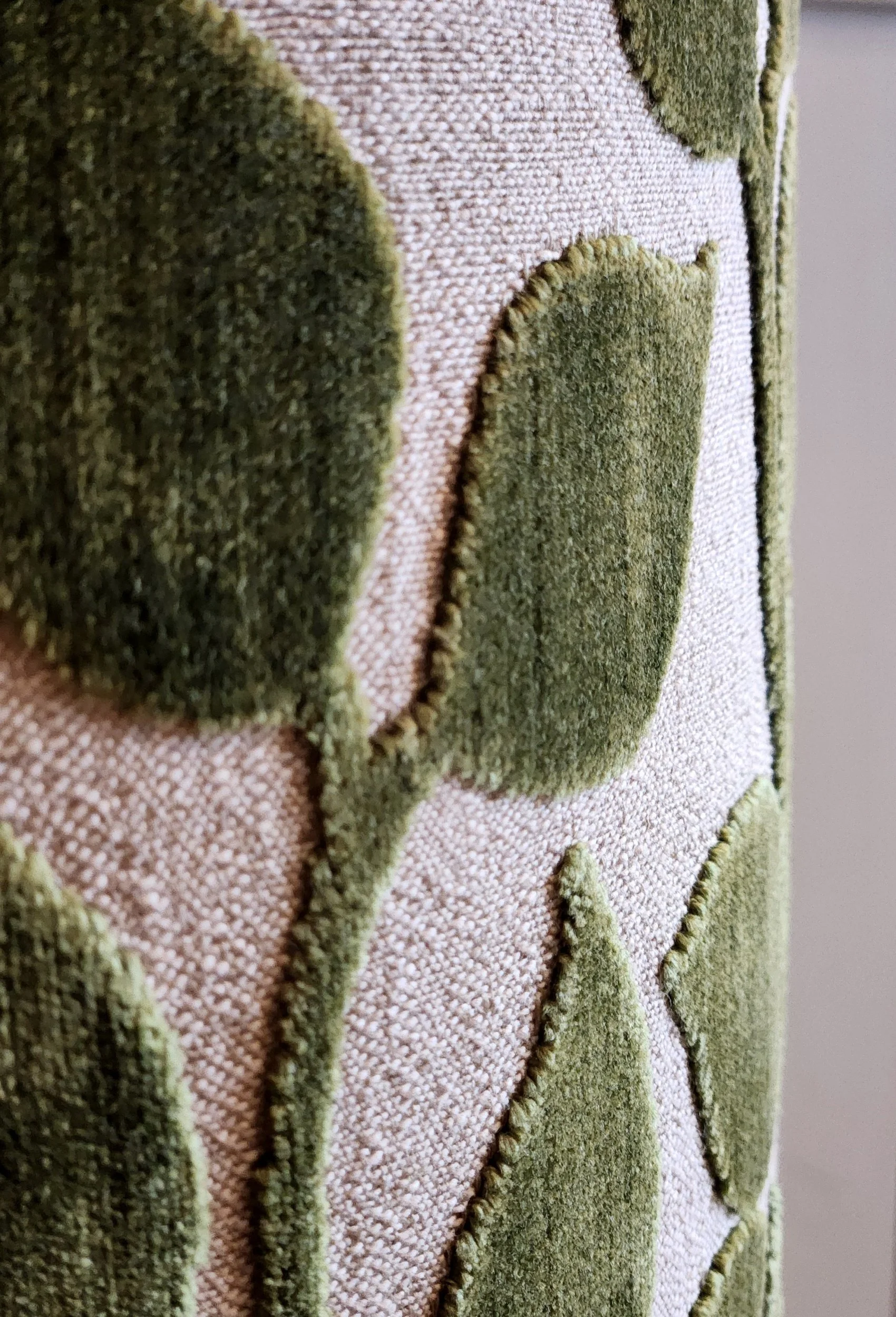 Close-up of a textile fabric with raised olive-green velvet leaves on a beige background.