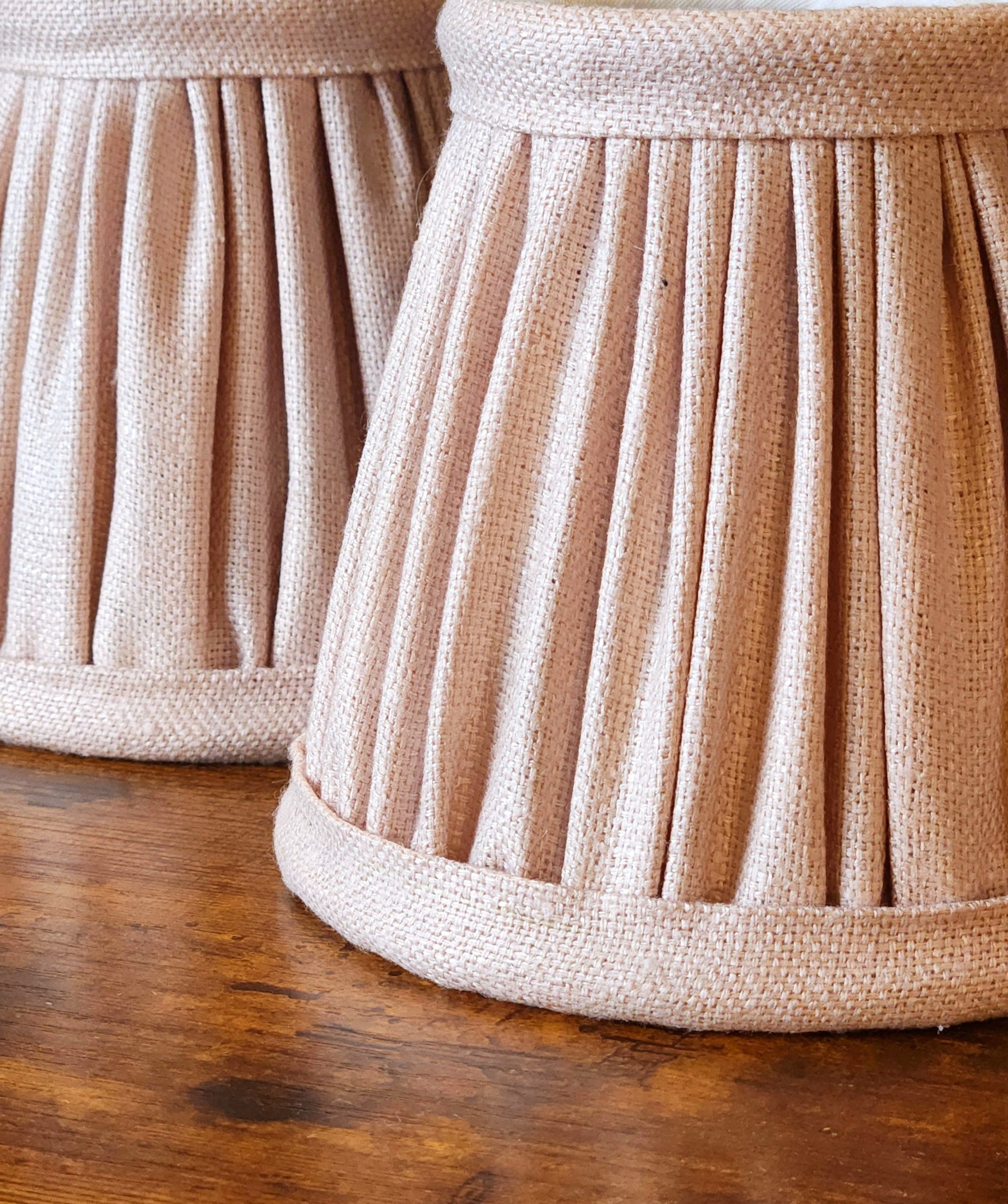 Close-up view of blush pink pleated fabric on a mini lampshade, resting on a wooden surface.