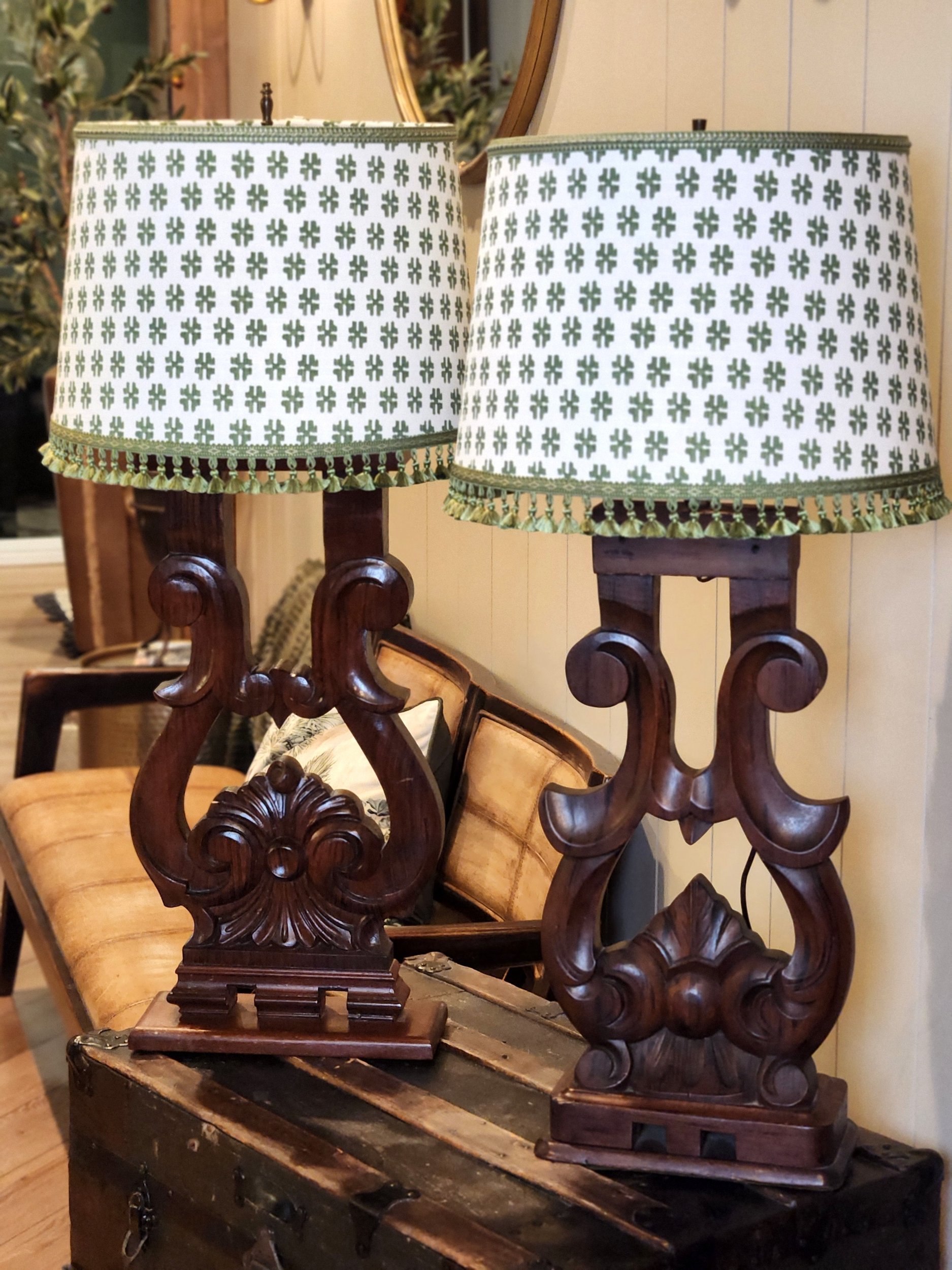 Pair of vintage wooden table lamps with carved bases and green and white patterned fabric lampshades placed on a wooden chest.
