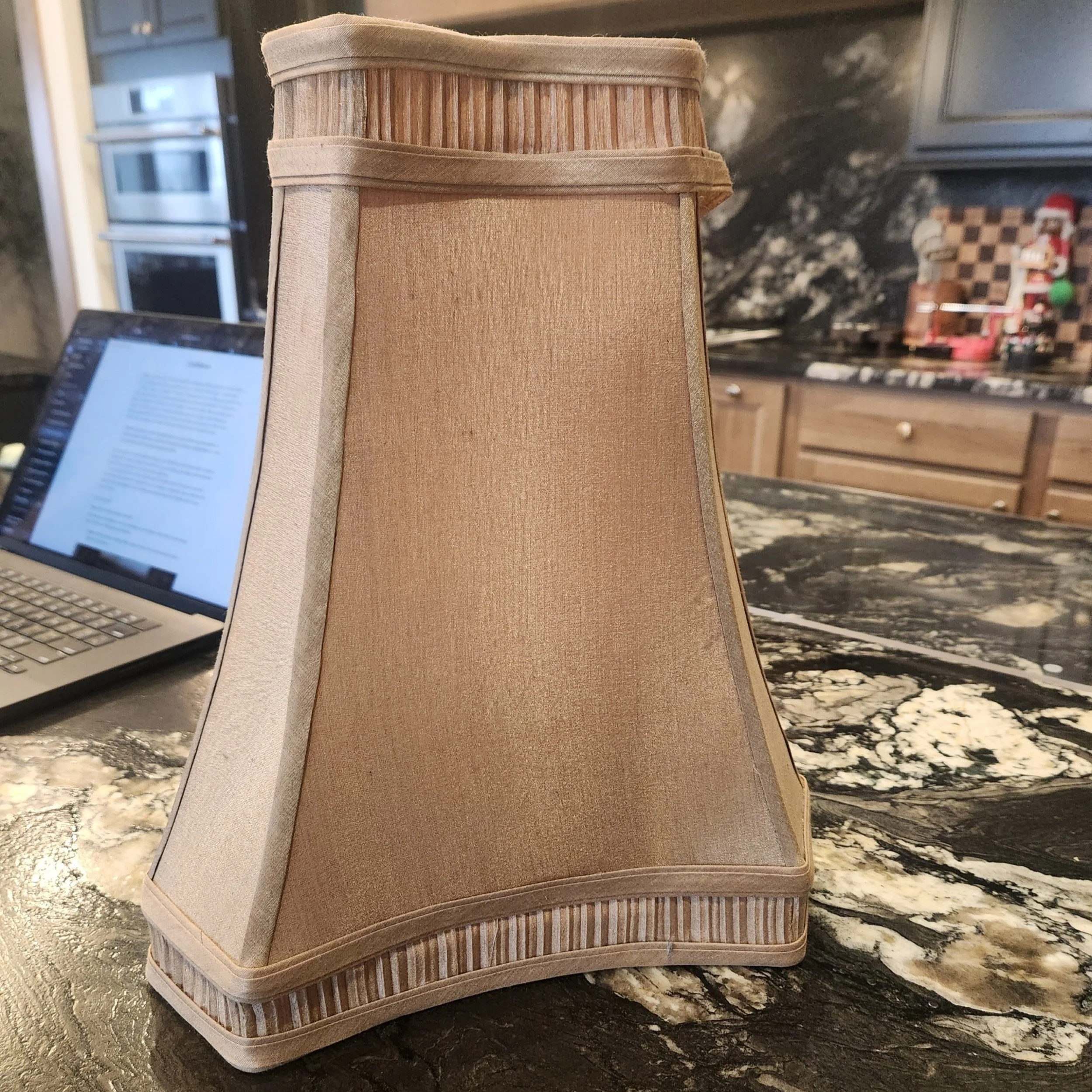 Beige fabric lampshade with a valance trim on a marble countertop.