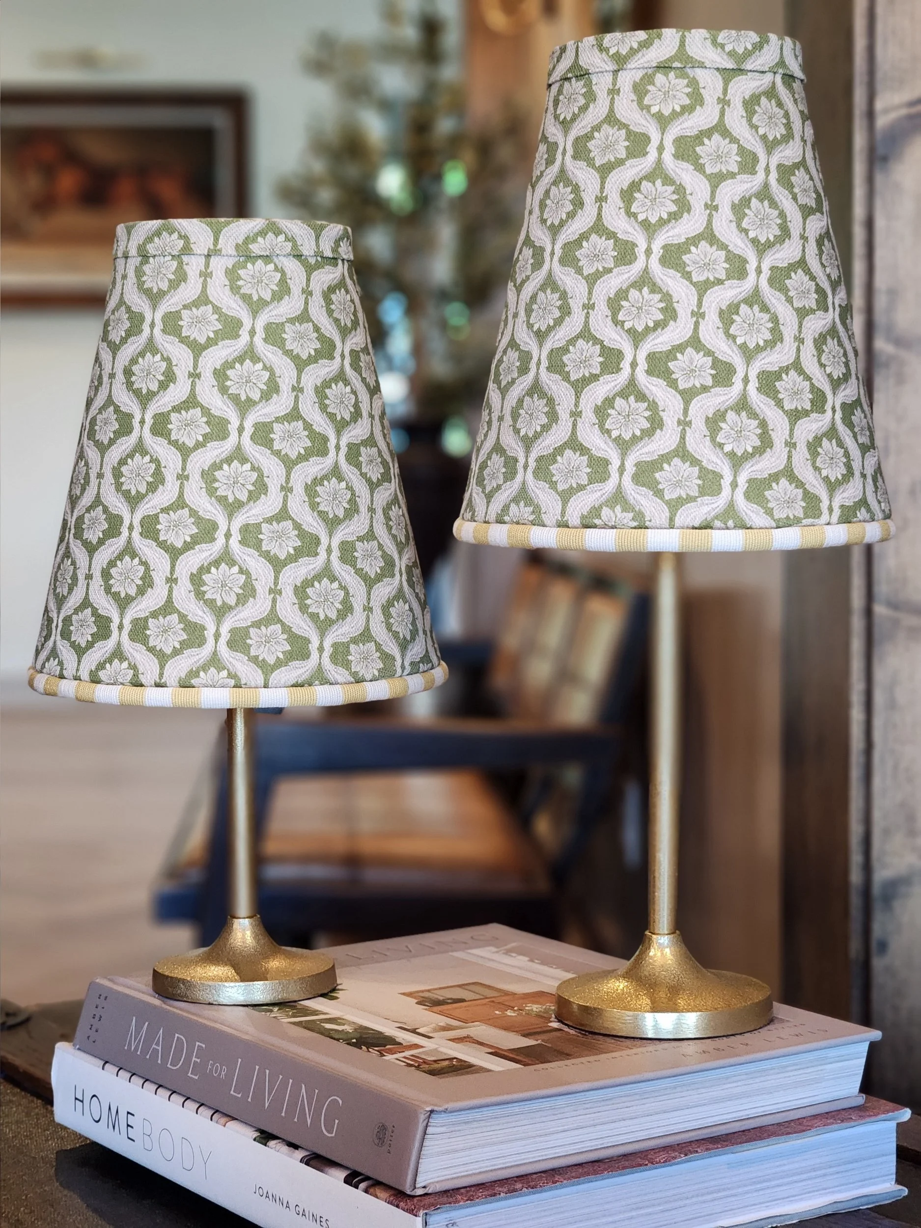Two decorative sconce lamps with floral-patterned shades and gold bases sit on top of interior design books.