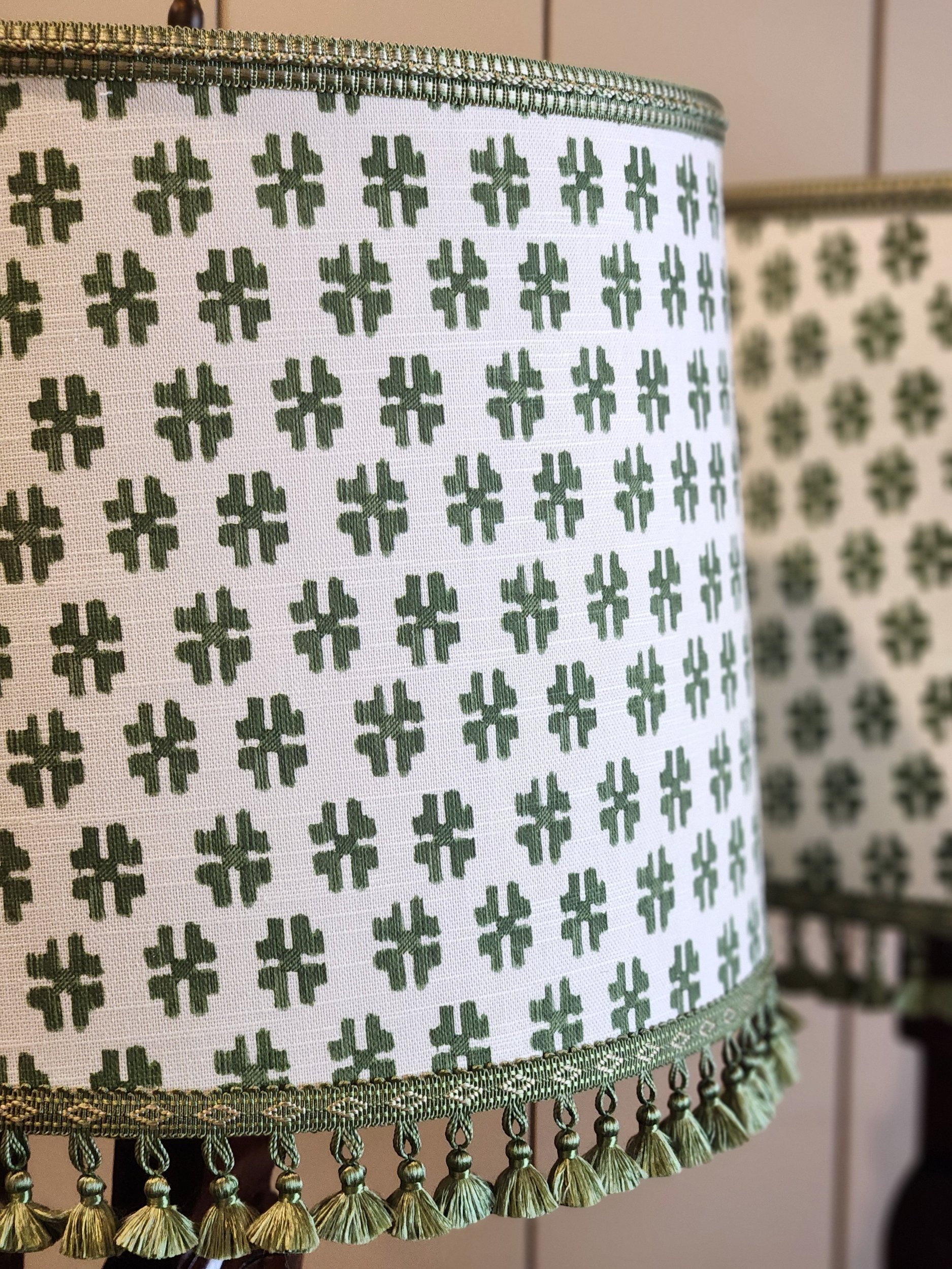 Close-up of a white lampshade with a repeating green clover pattern and a green trim with small tassels at the bottom.