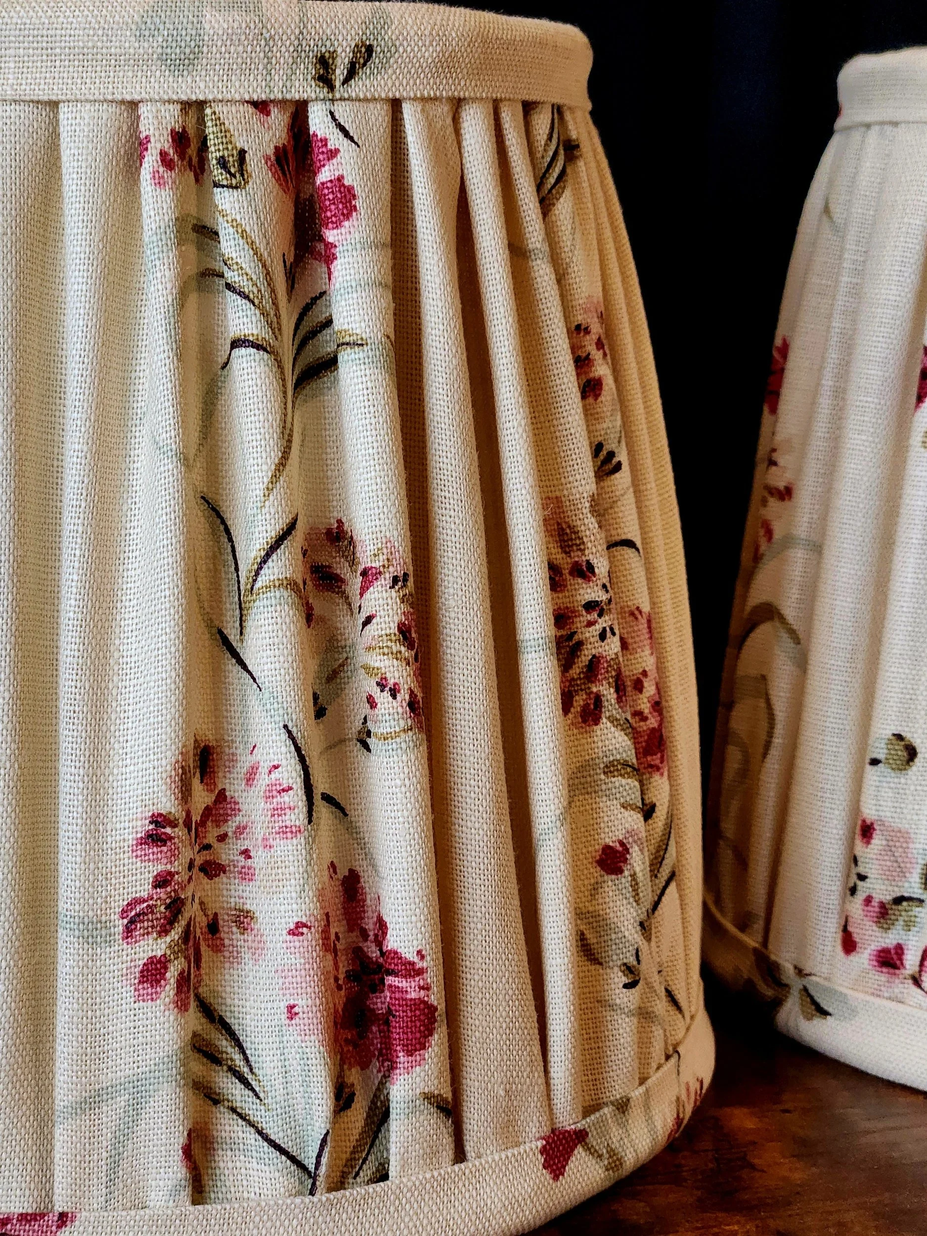 Close-up of a cream-colored fabric lampshade with a pink floral and black vine pattern.