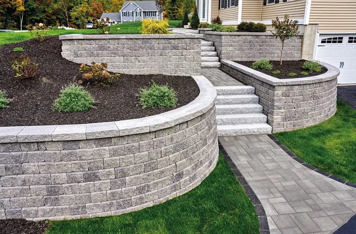 Green Gorilla Created a landscaped front yard with tiered stone retaining walls, a curved brick walkway, and small trees and shrubs.