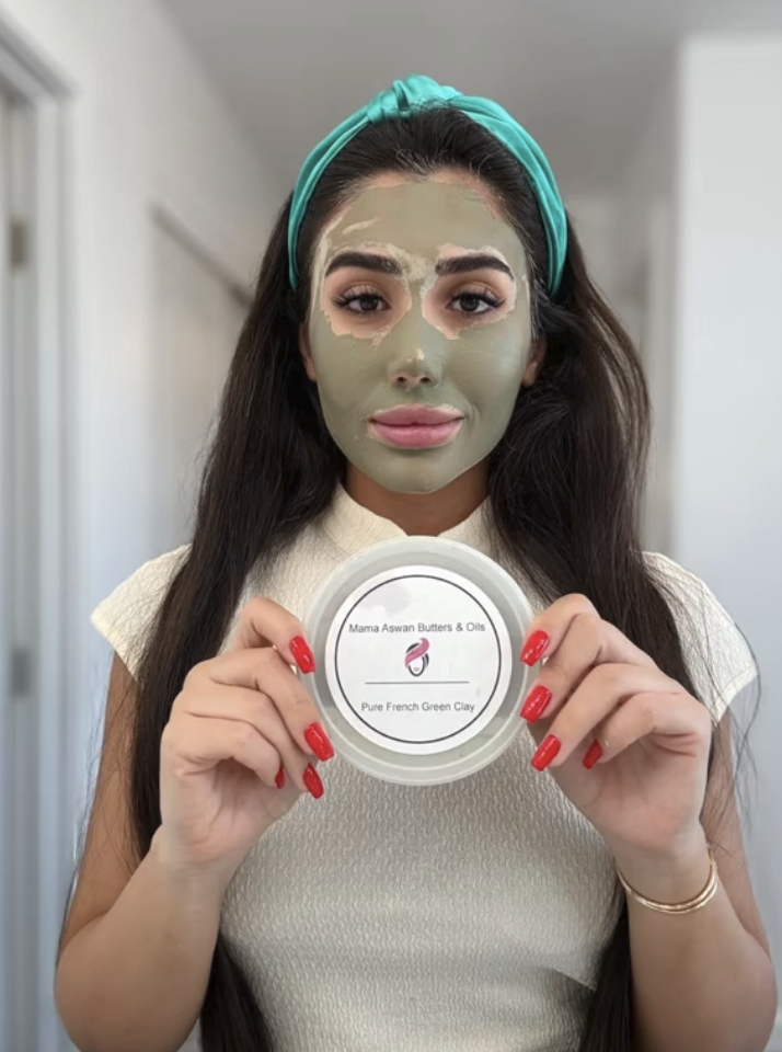 Woman wearing a green clay facial mask and holding a container of Mama Aswan Pure French Green Clay.
