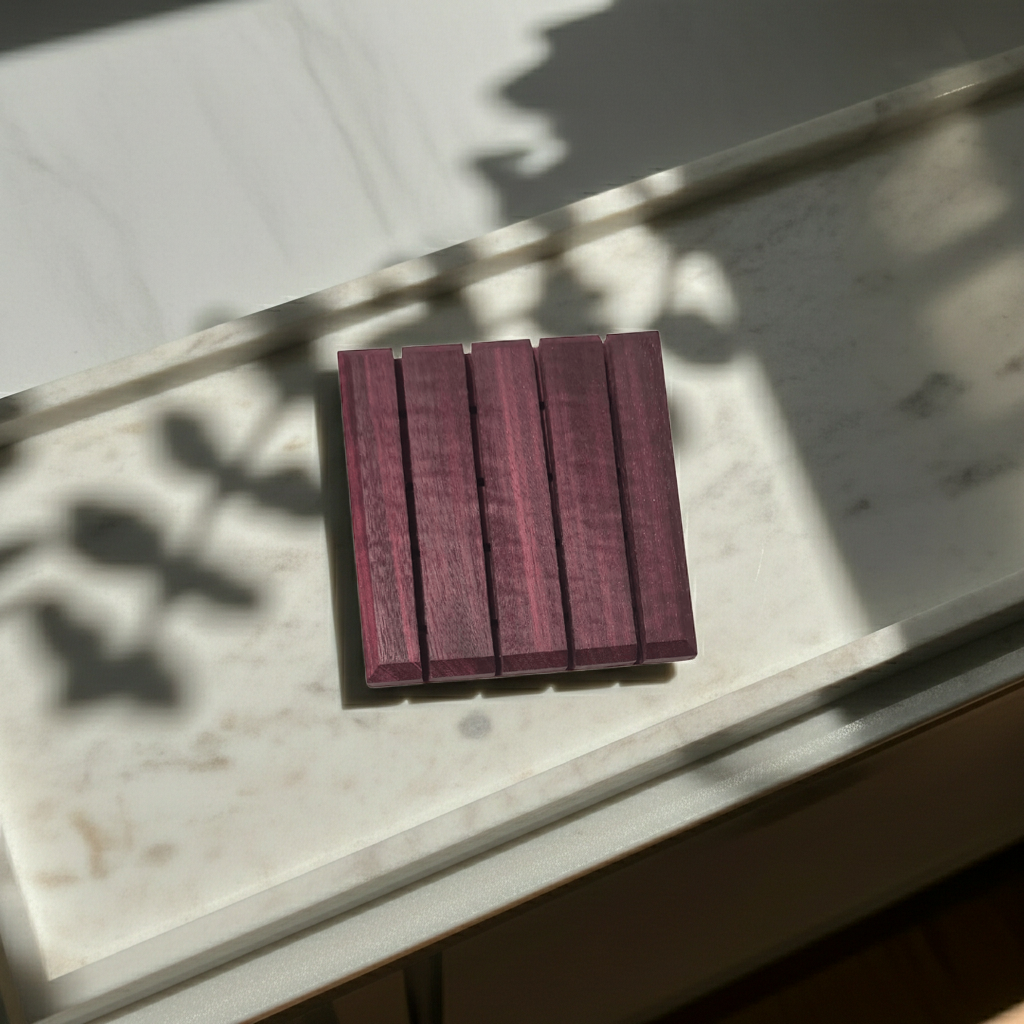 Purple Heart wood soap dish lying flat on a marble tray with dappled plant shadows in sunlight.