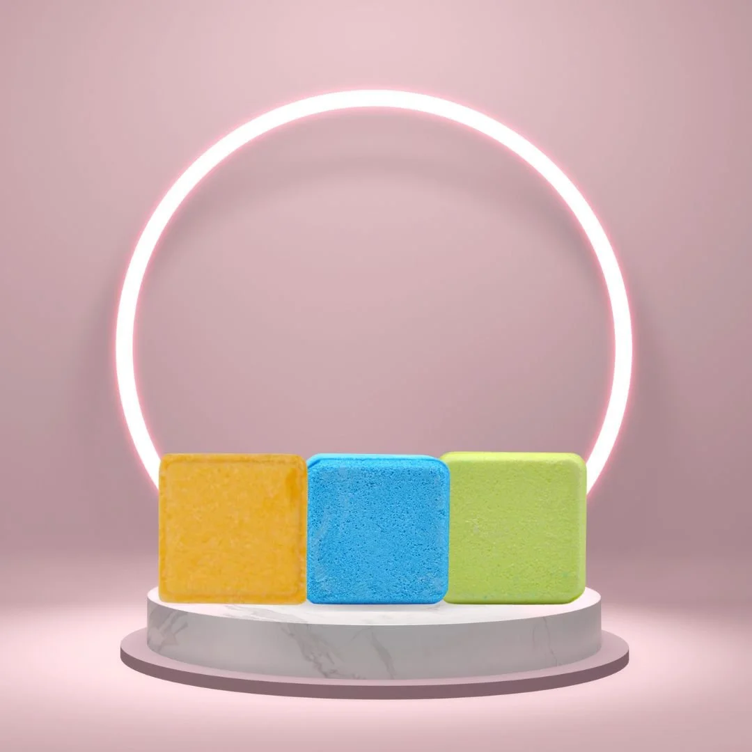 Large Shower Steamers in yellow, blue, and green on a white pedestal with a glowing pink circle background.