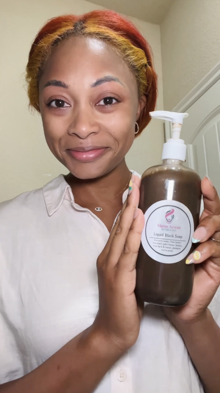 Woman smiling and holding a bottle of Mama Aswan Liquid Black Soap with the product label facing the camera.
