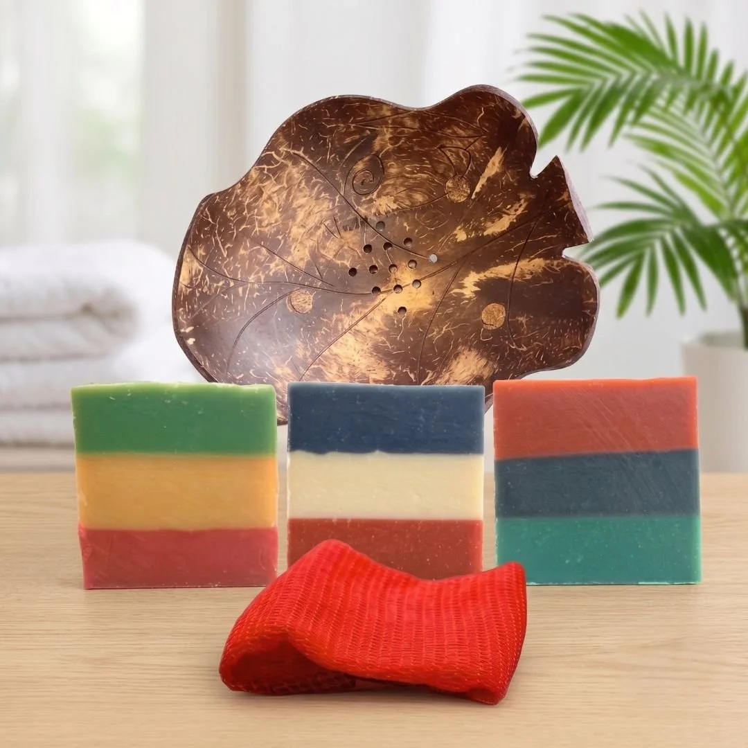 Full Heritage Trifecta Shower Set with three Heritage Line soaps, Coconut Shell Soap Dish, and red Sapo Sponge on a light wood surface.