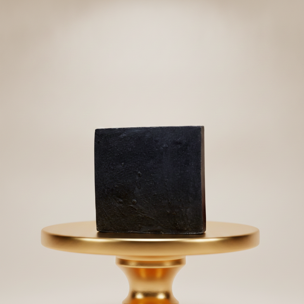 Black Soap Bar displayed on a gold pedestal with a soft neutral background.