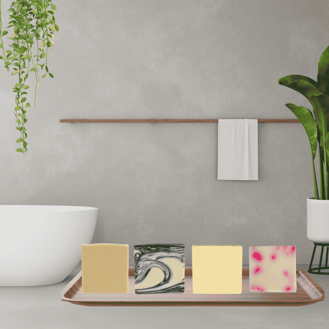 Modern spa bathroom scene with four artisan soap bars in yellow, black-and-white swirl, creamy beige, and pink with red specks—handcrafted natural soaps by Mama Aswan Butters & Oils.