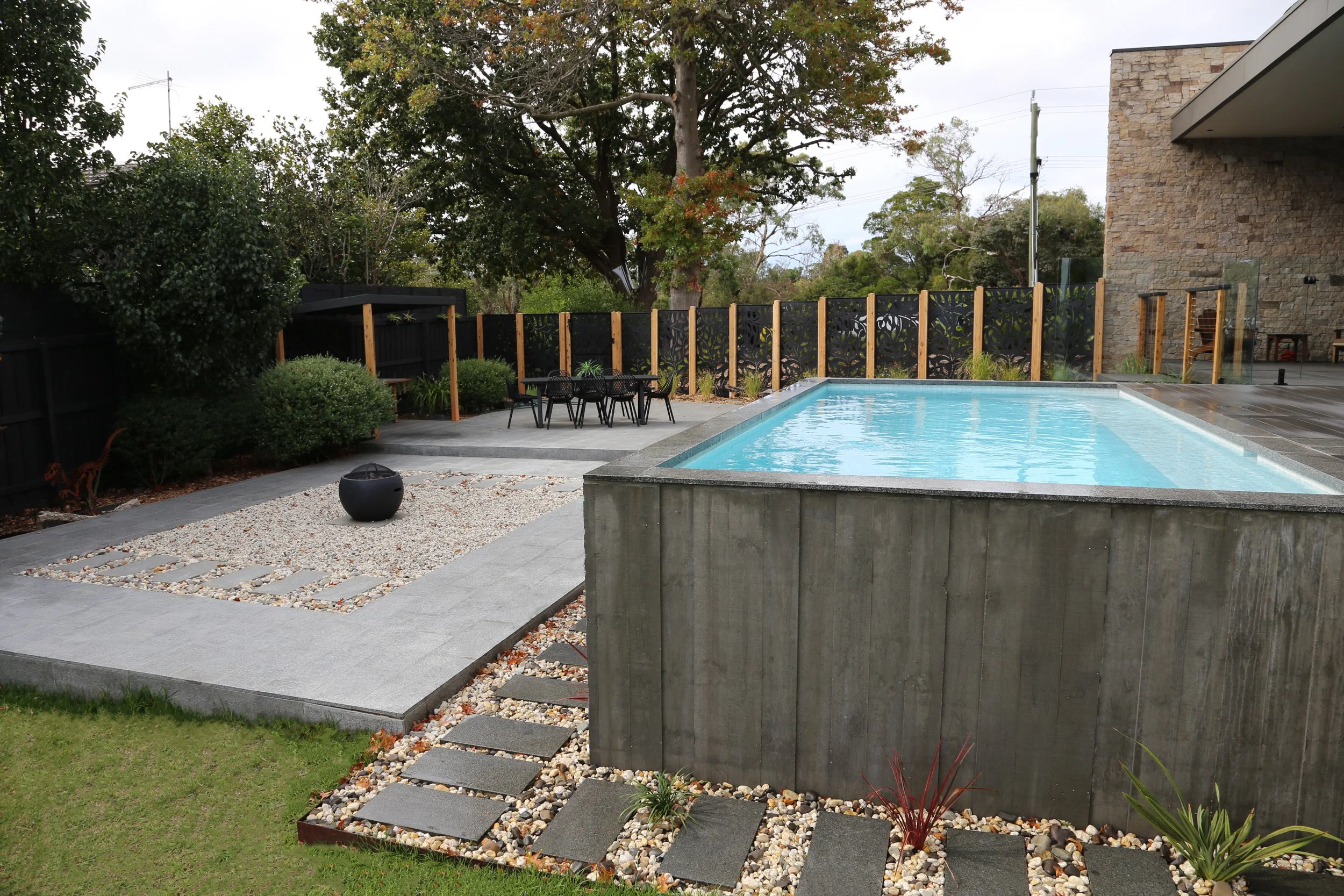 Side view of a luxurious rustic above ground pool in Mount Eliza (Mt Eliza) on the Mornington Peninsula with blue water and wooden decking surrounding it.