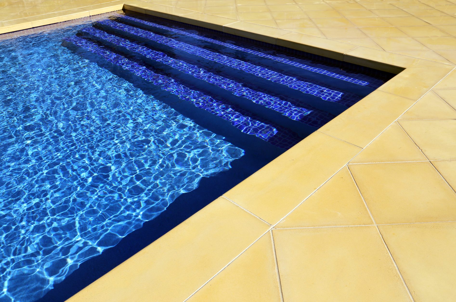 Close up view of the stairs of a luxurious french style in-ground pool and spa in Frankston South with deep blue water sand coloured pavers.