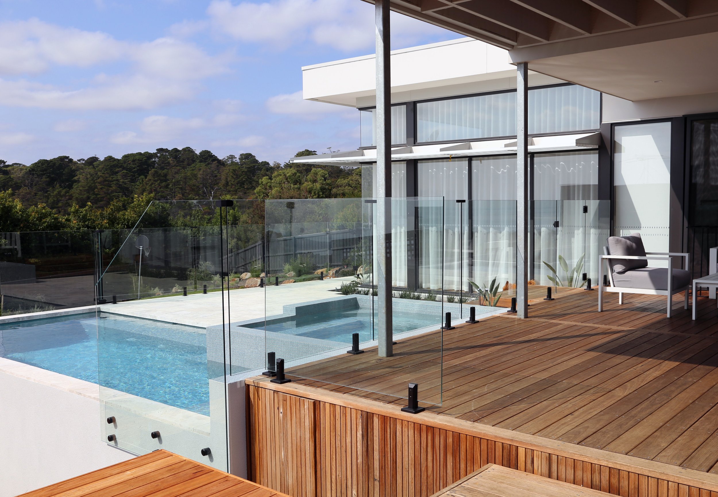 Larger side view of a luxurious pool in Mount Martha on the Mornington Peninsula with white pavers, blue water and wooden decking surrounding it.