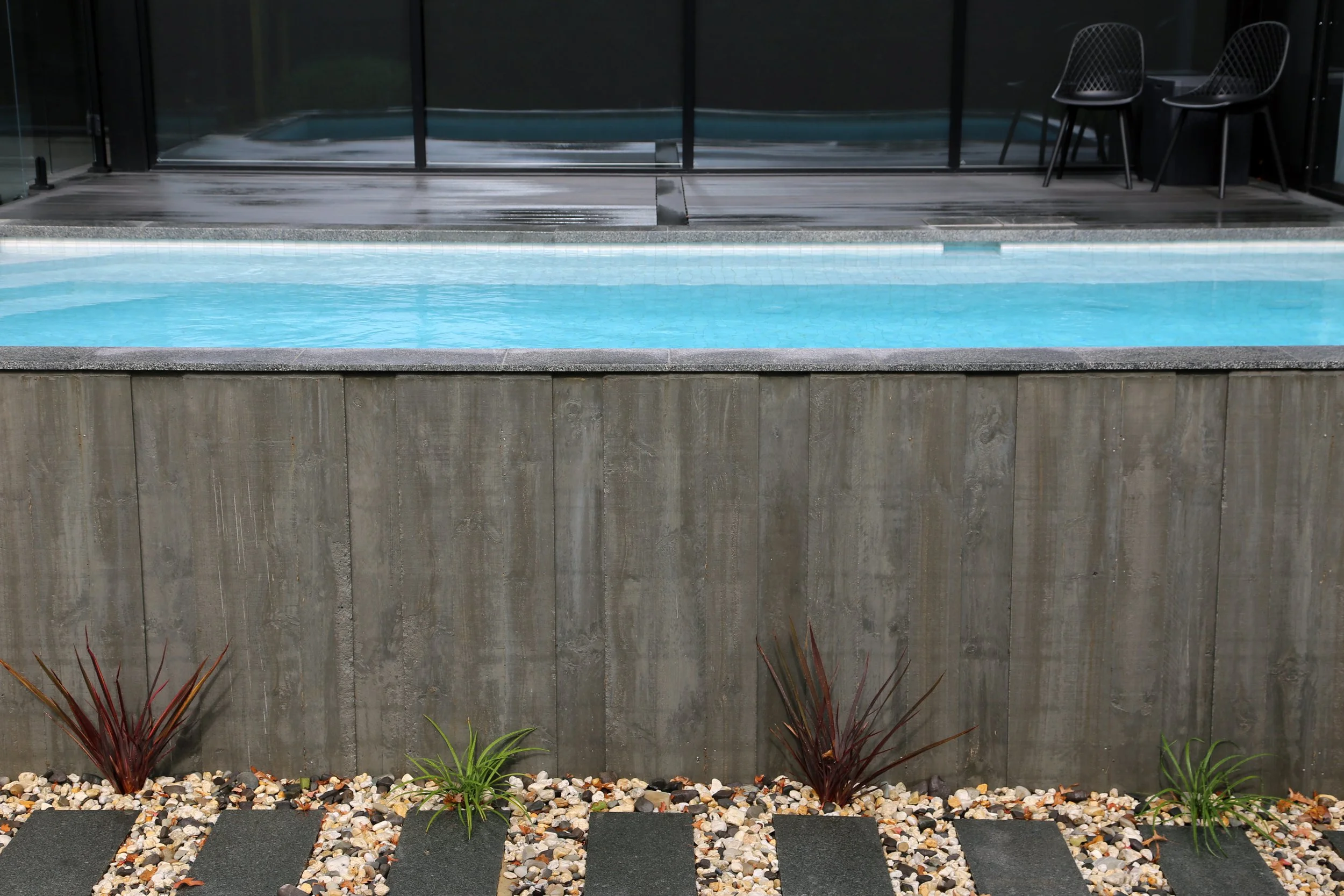 Other side view of a luxurious rustic above ground pool in Mount Eliza (Mt Eliza) on the Mornington Peninsula with blue water and wooden decking surrounding it.