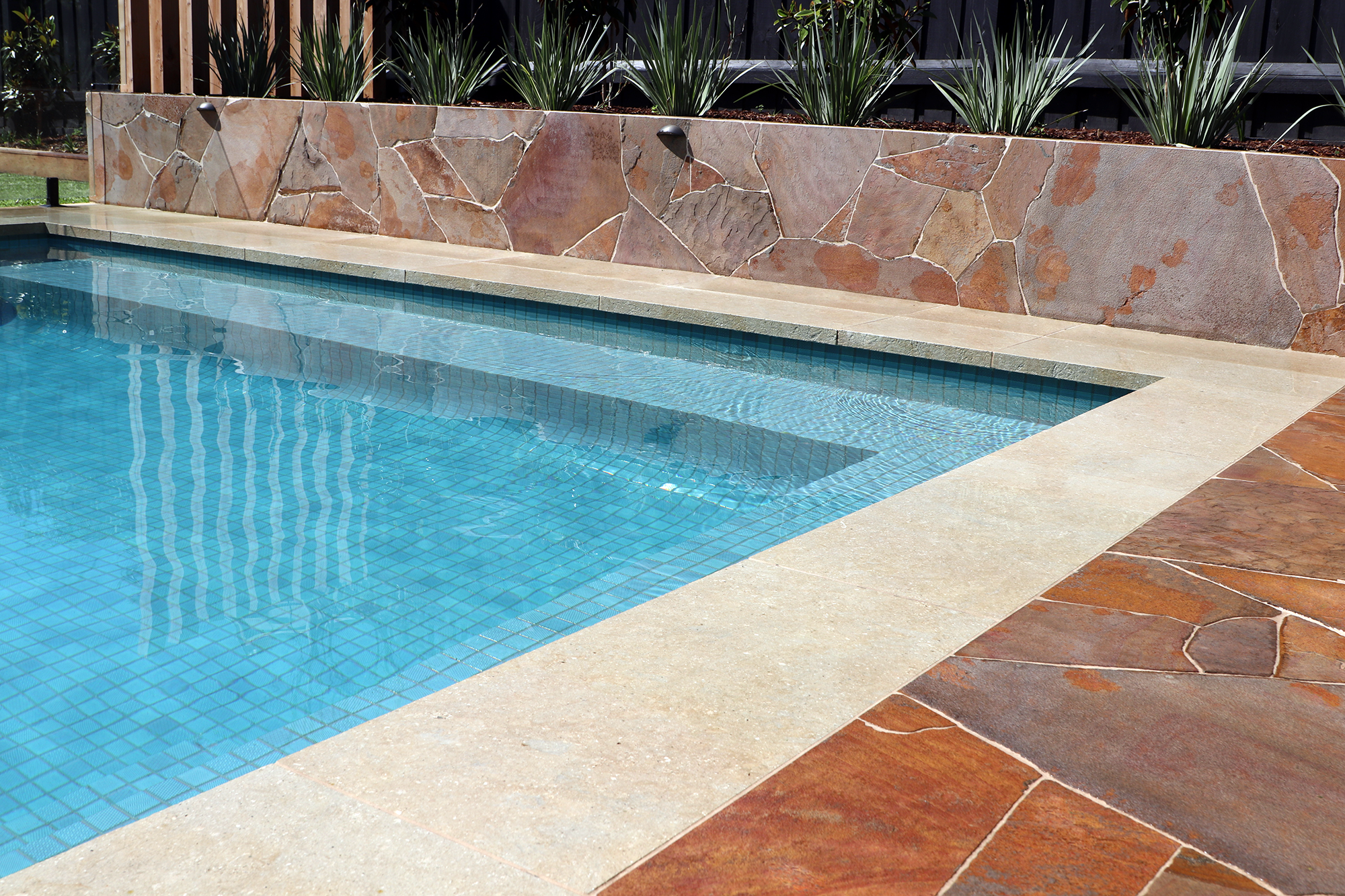 Close view of a family in-ground pool in Mount Eliza (Mt Eliza) on the Mornington Peninsula with blue water, natural rock pavers and a barbecue decking sitting area.