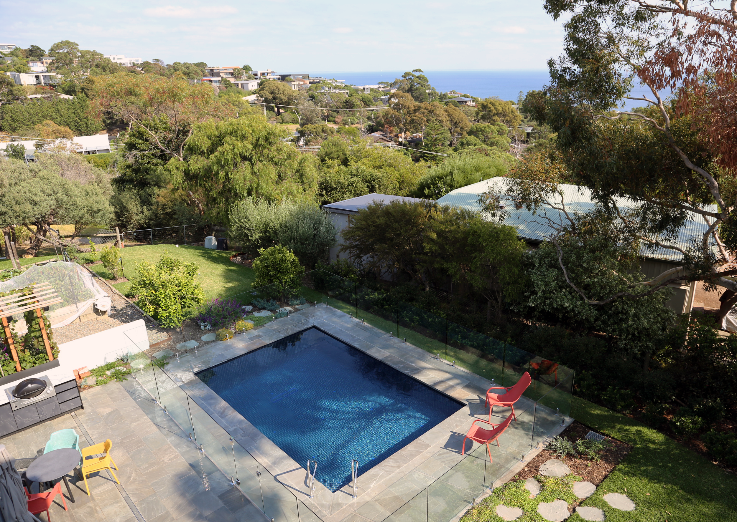 Top view of a luxurious beach side in-ground pool in Mount Eliza (Mt Eliza) on the Mornington Peninsula with blue water and a barbecue sitting area.
