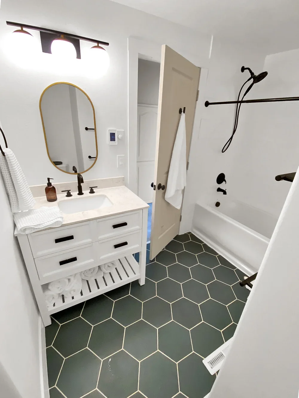 Modern bathroom with white vanity, black fixtures, black hex tile floor, and walk-in shower with black fixtures and a black showerhead.