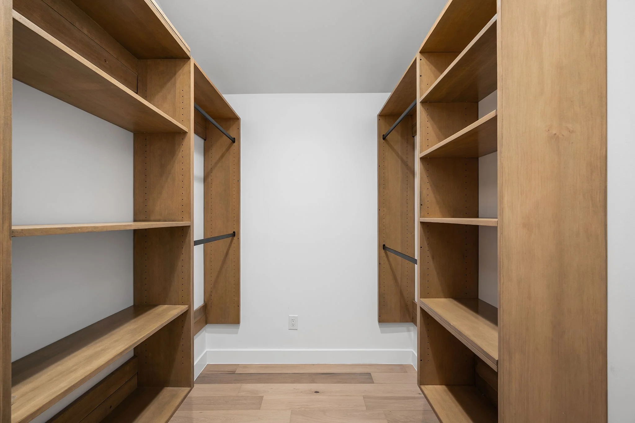 Empty walk-in closet with wooden shelves and hanging rods.