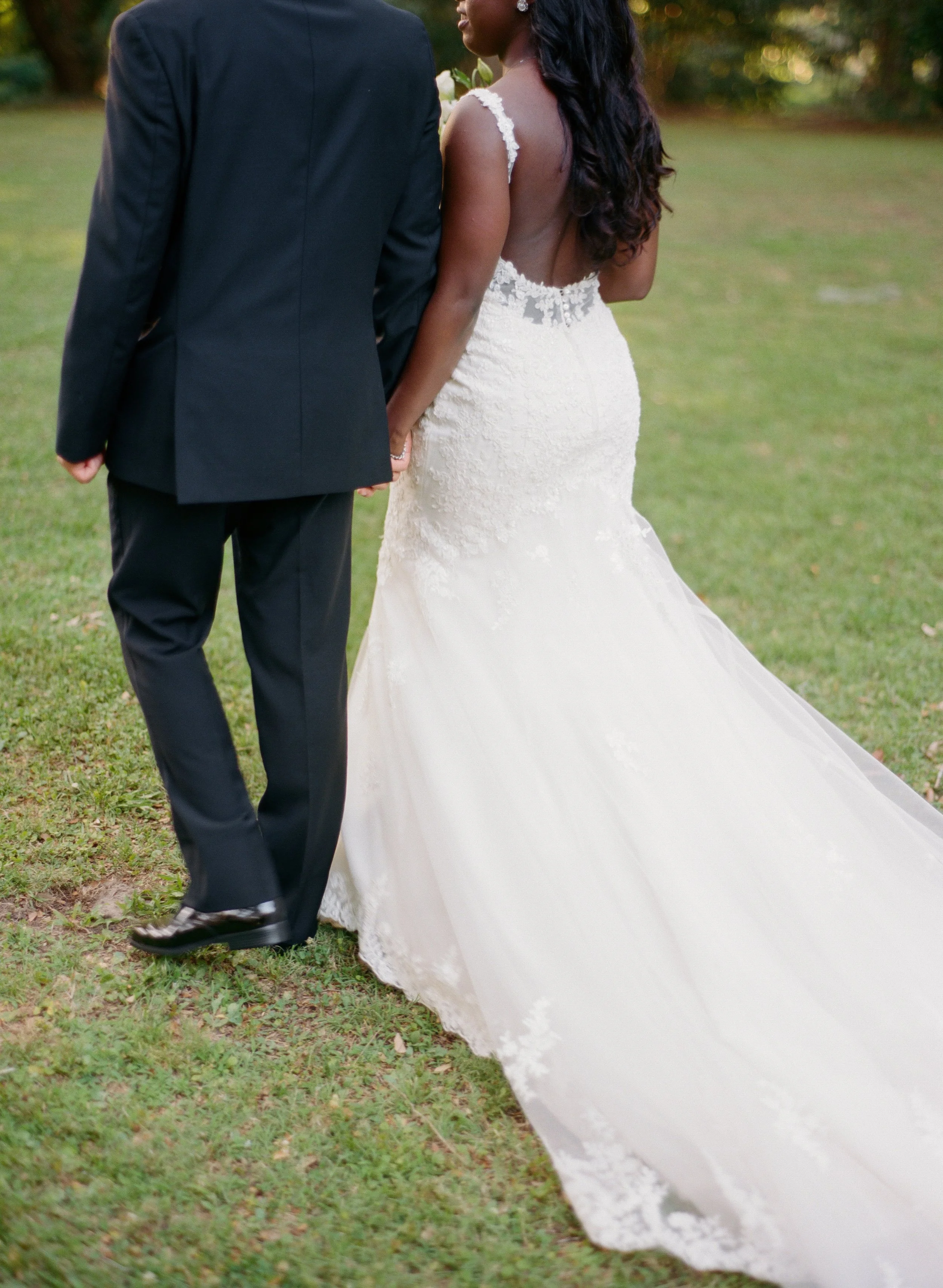 Interracial couple walking hand in hand in Charleston with bride’s lace wedding dress detail captured on film