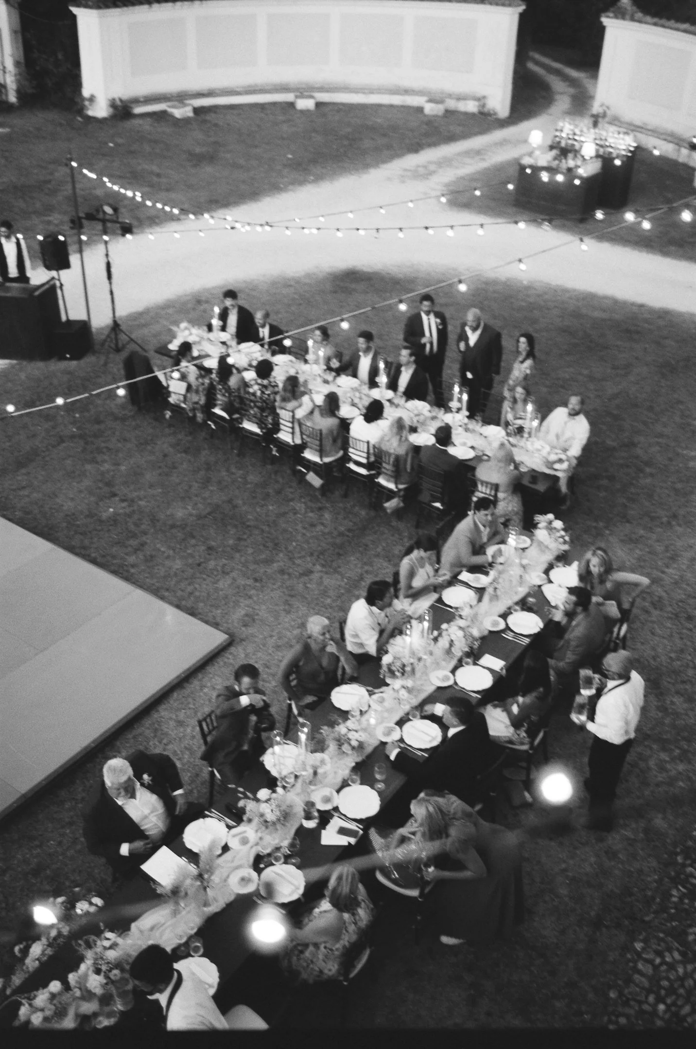 An outdoor evening wedding reception at Villa Pianciani in italy, with guests seated at long decorated tables, string lights overhead, a dance floor, and a buffet table in the background.