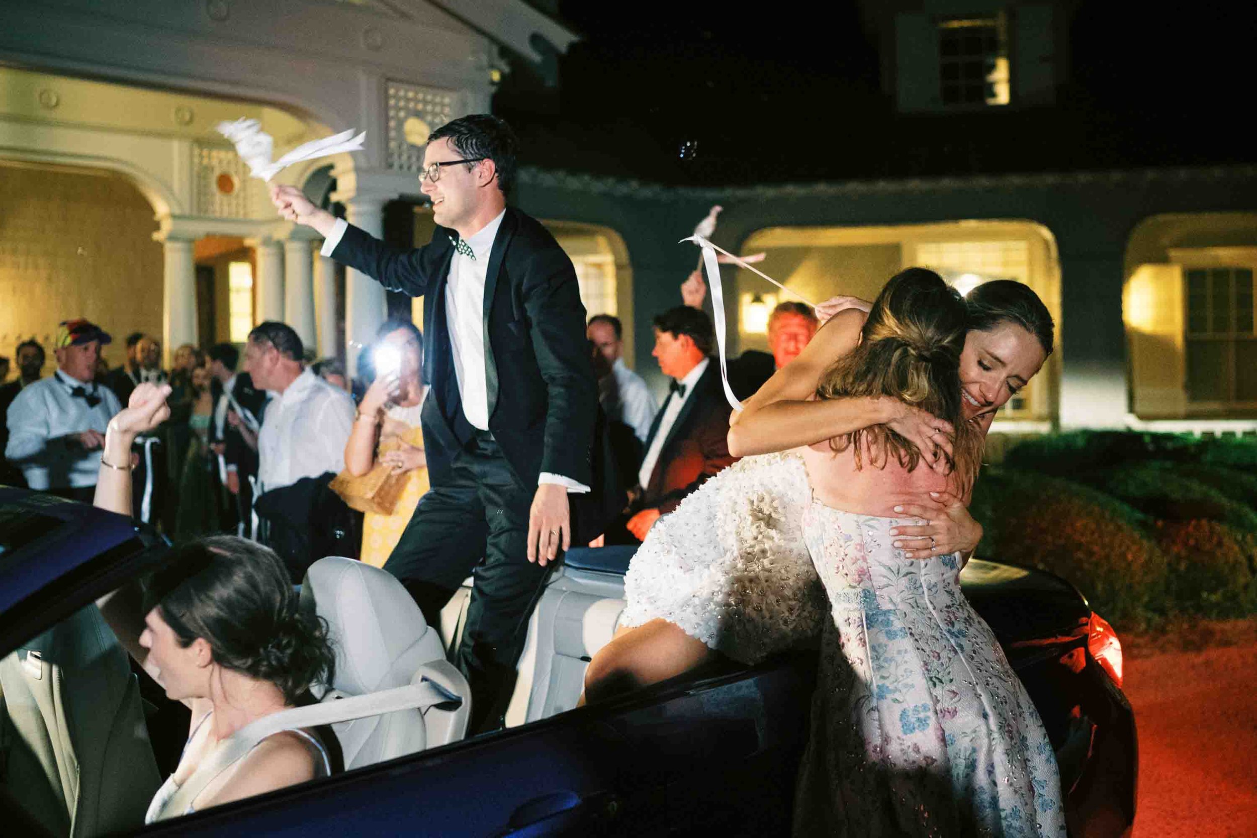 Bride and groom celebrating during their wedding exit in a convertible car at night