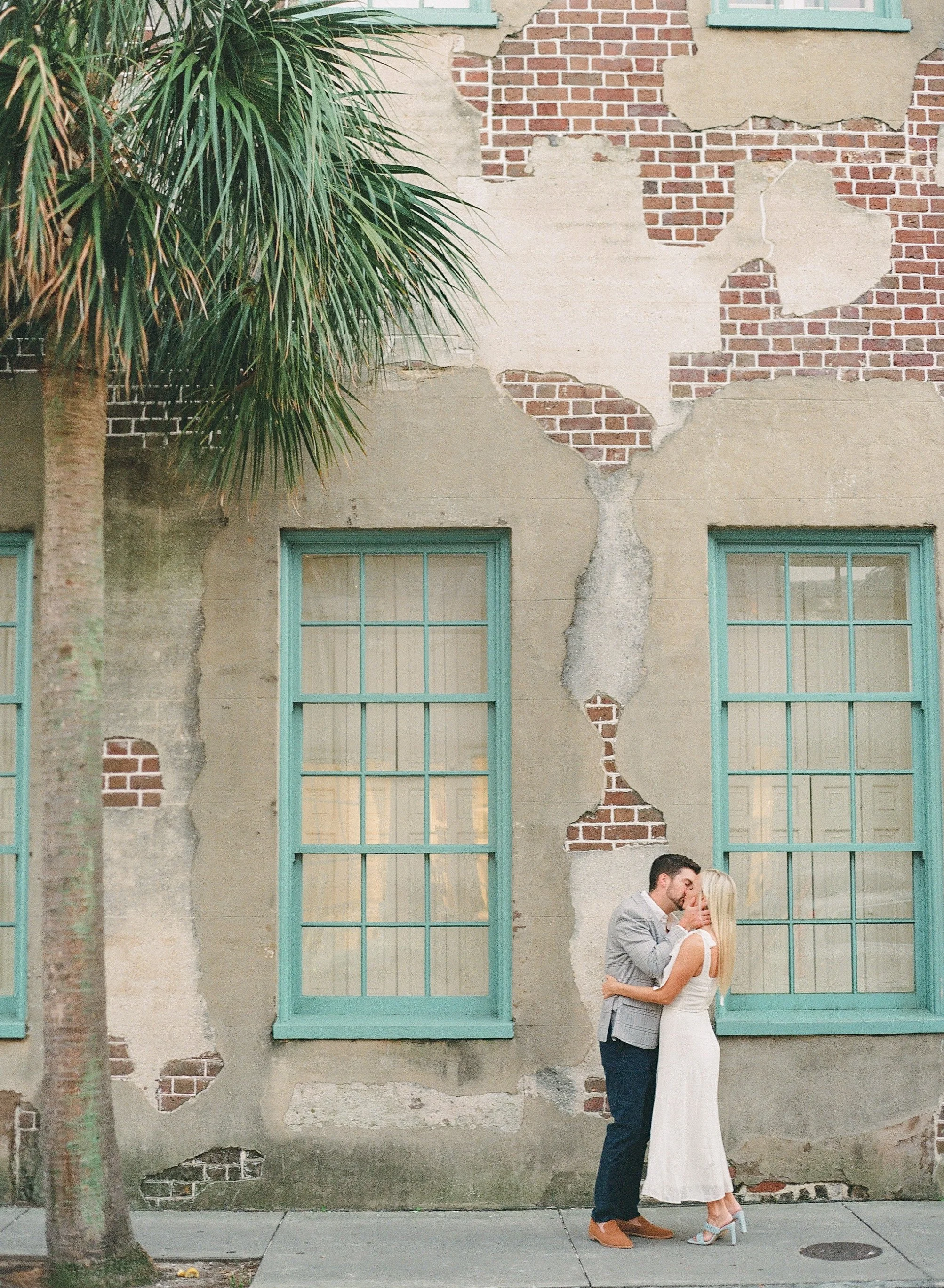 engagement photos on Queen Street in Charleston with textured historic wall and palm tree