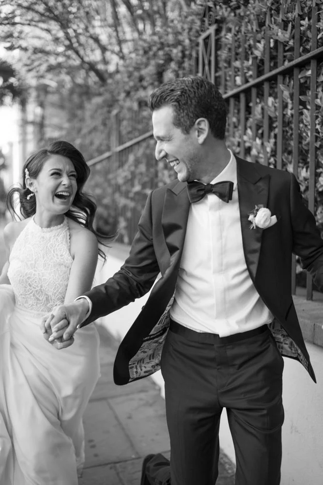 Black and white editorial portrait of bride and groom laughing while running outside of the William Aiken House in Charleston