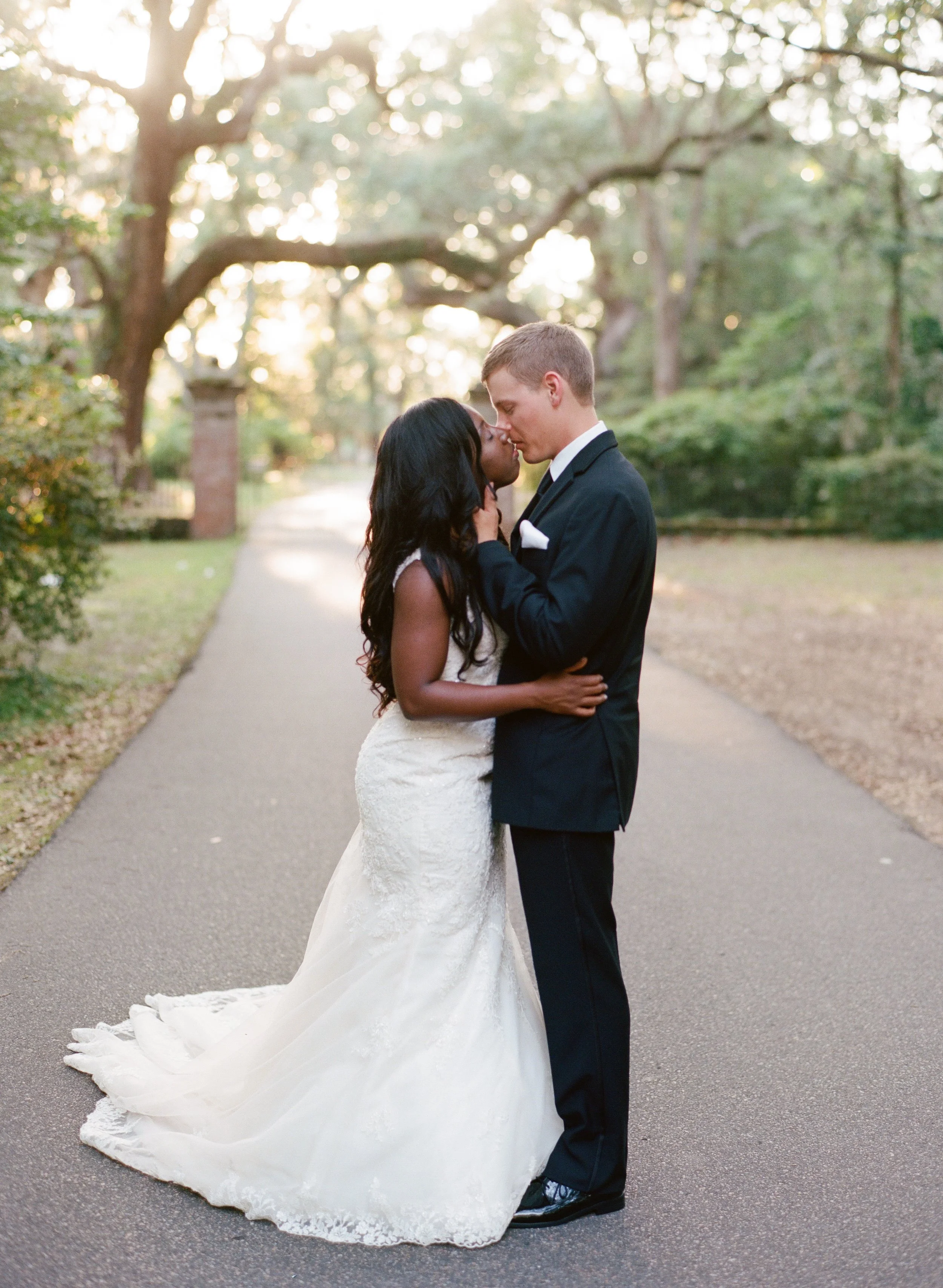 Interracial bride and groom portrait on oak-lined path at Legare Waring House wedding in Charleston South Carolina”