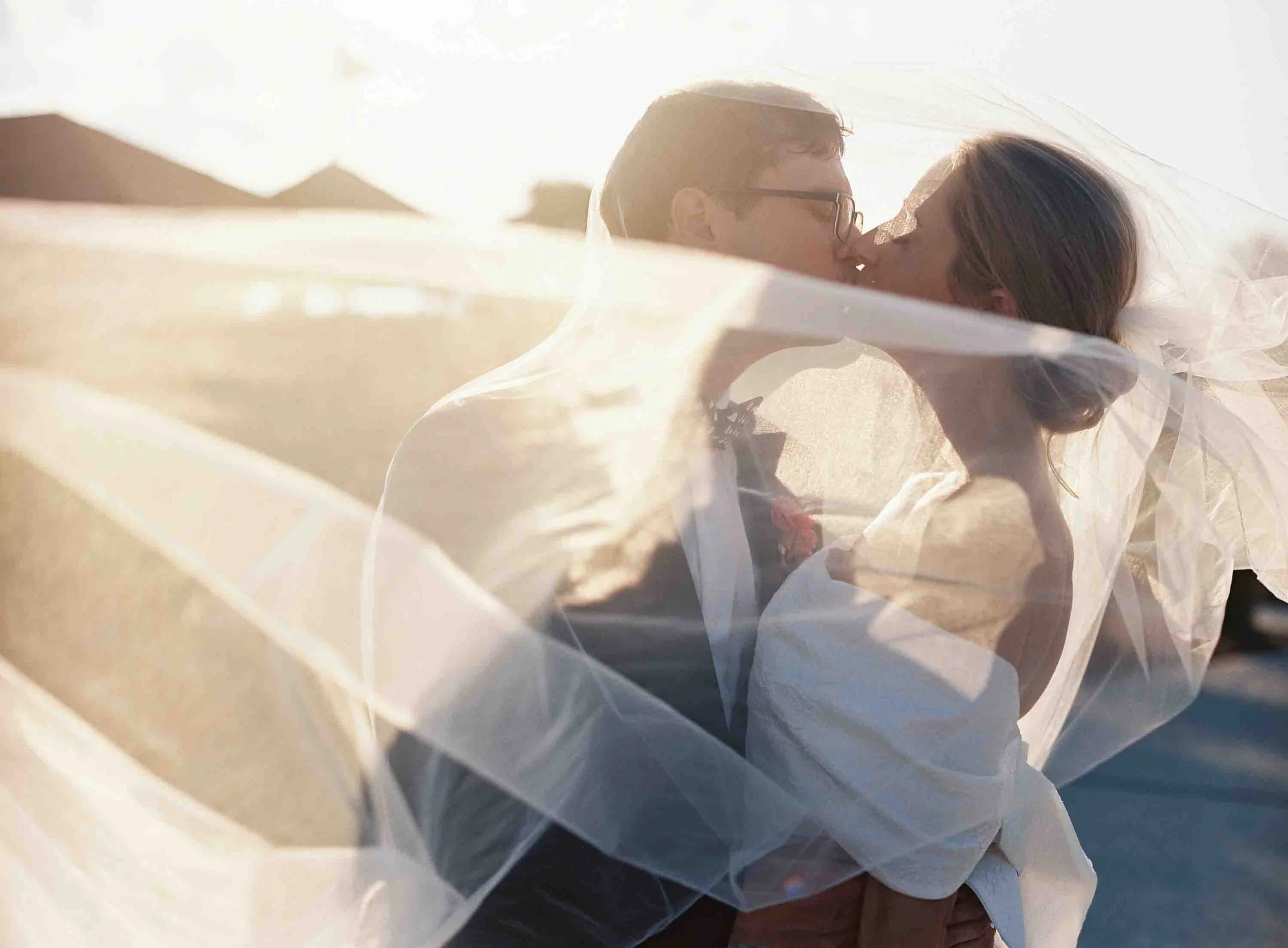 Bride and groom kissing through a flowing veil with soft sunset light at the Ocean Course