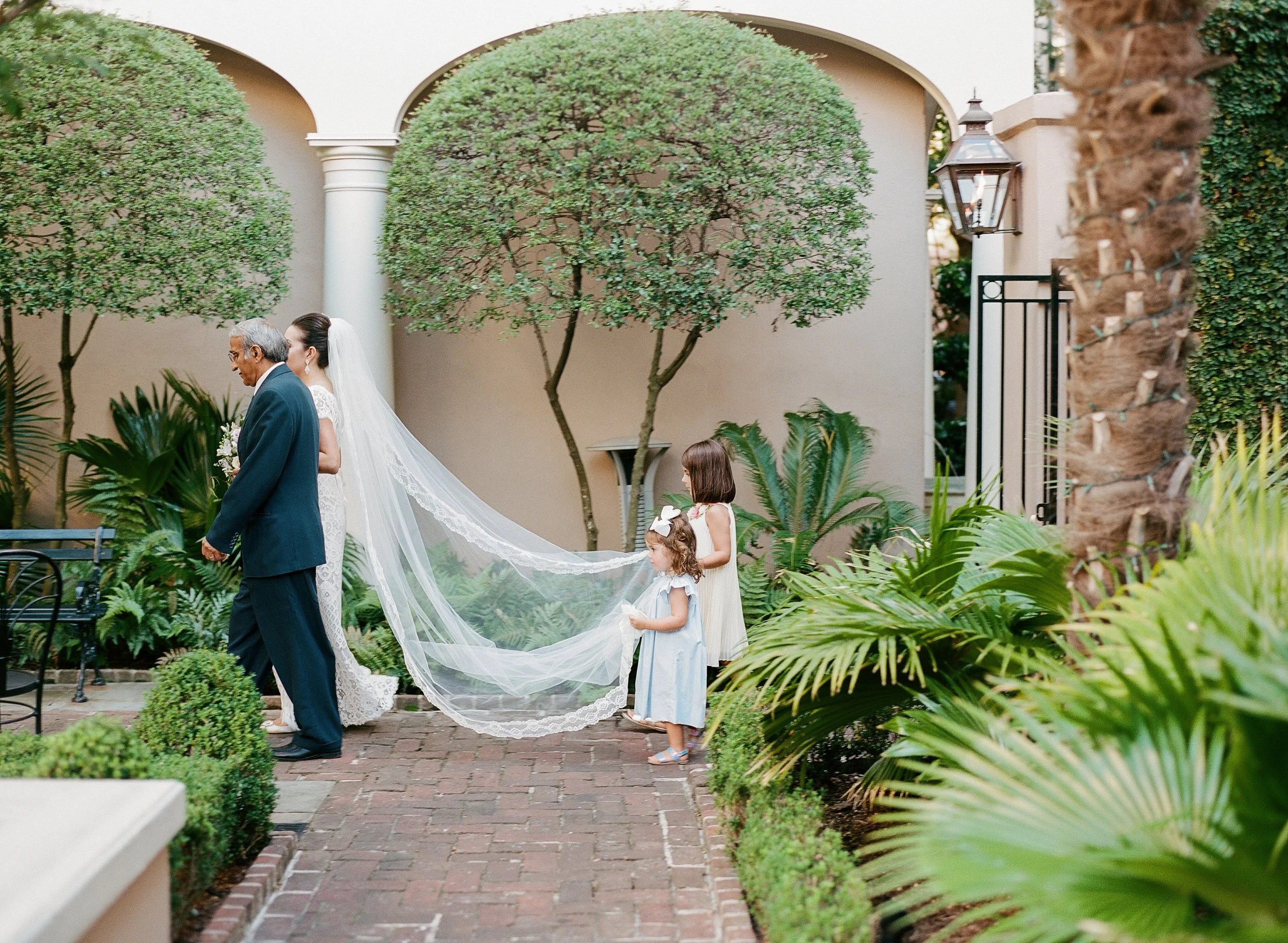 Flower girls hold the brides veil as she walks down the aisle during a Planters Inn wedding ceremony