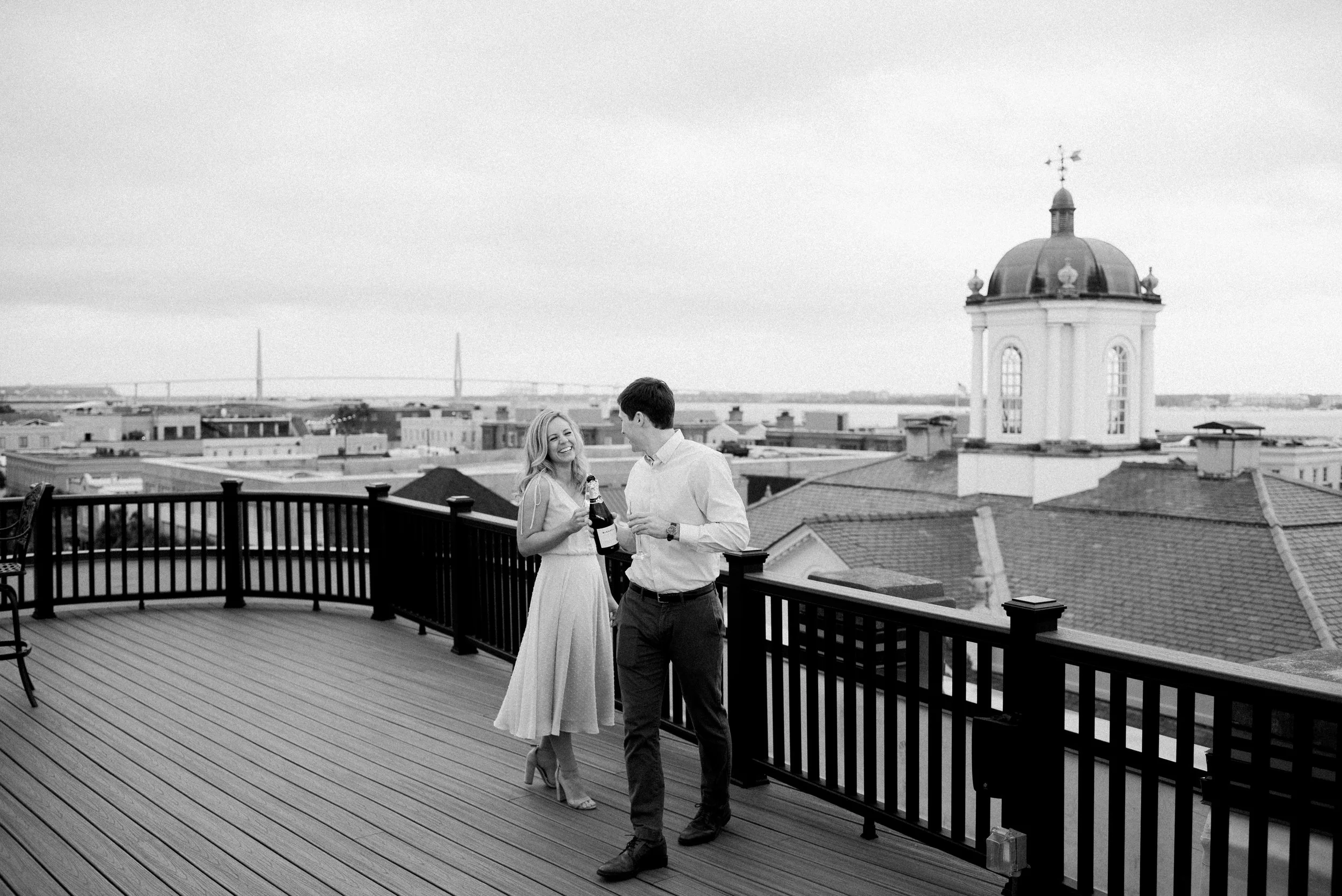 Newly engaged couple celebrates with champagne on rooftop on Broad Street in Charleston SC