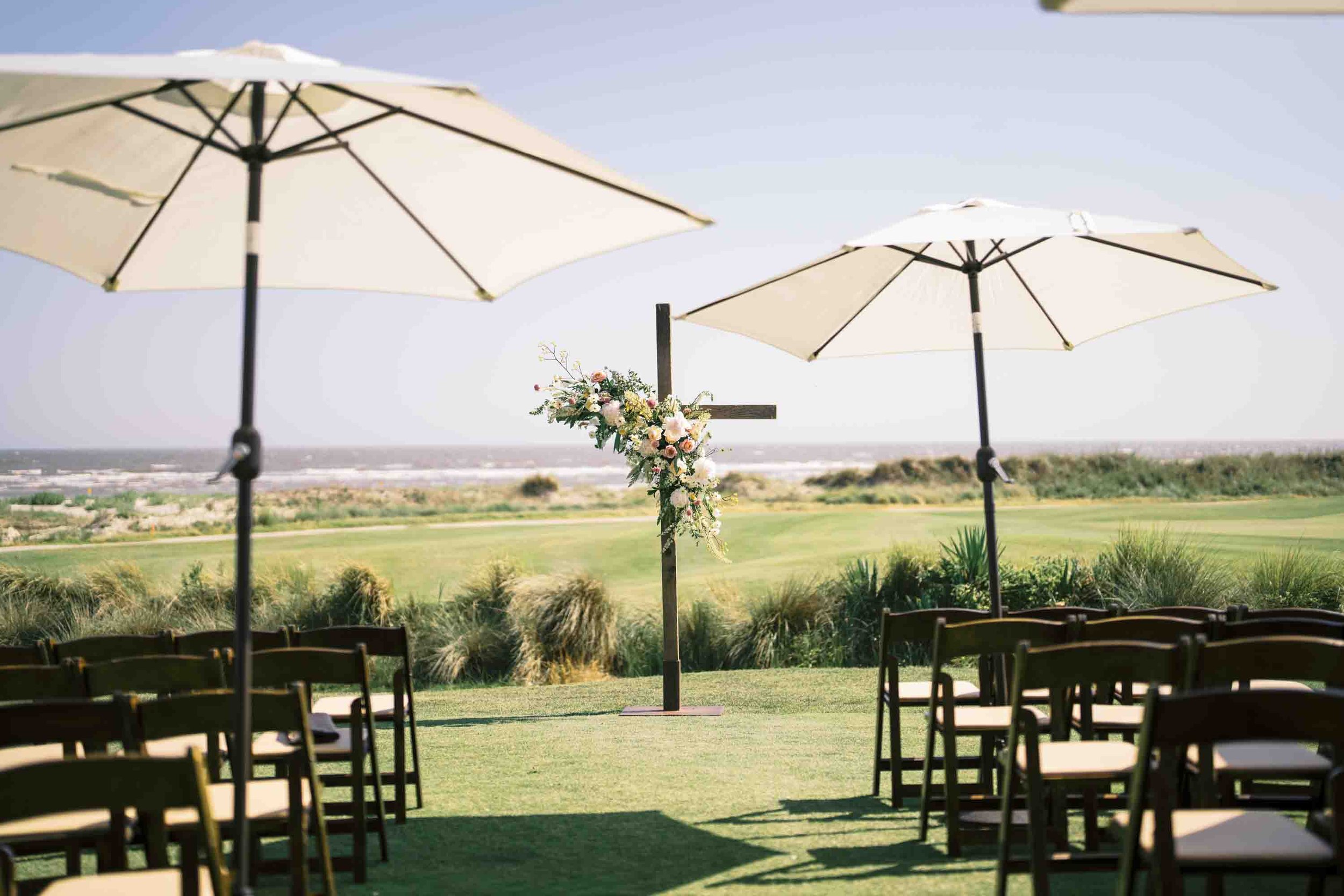 Outdoor wedding ceremony setup with floral cross overlooking the ocean at Kiawah Island