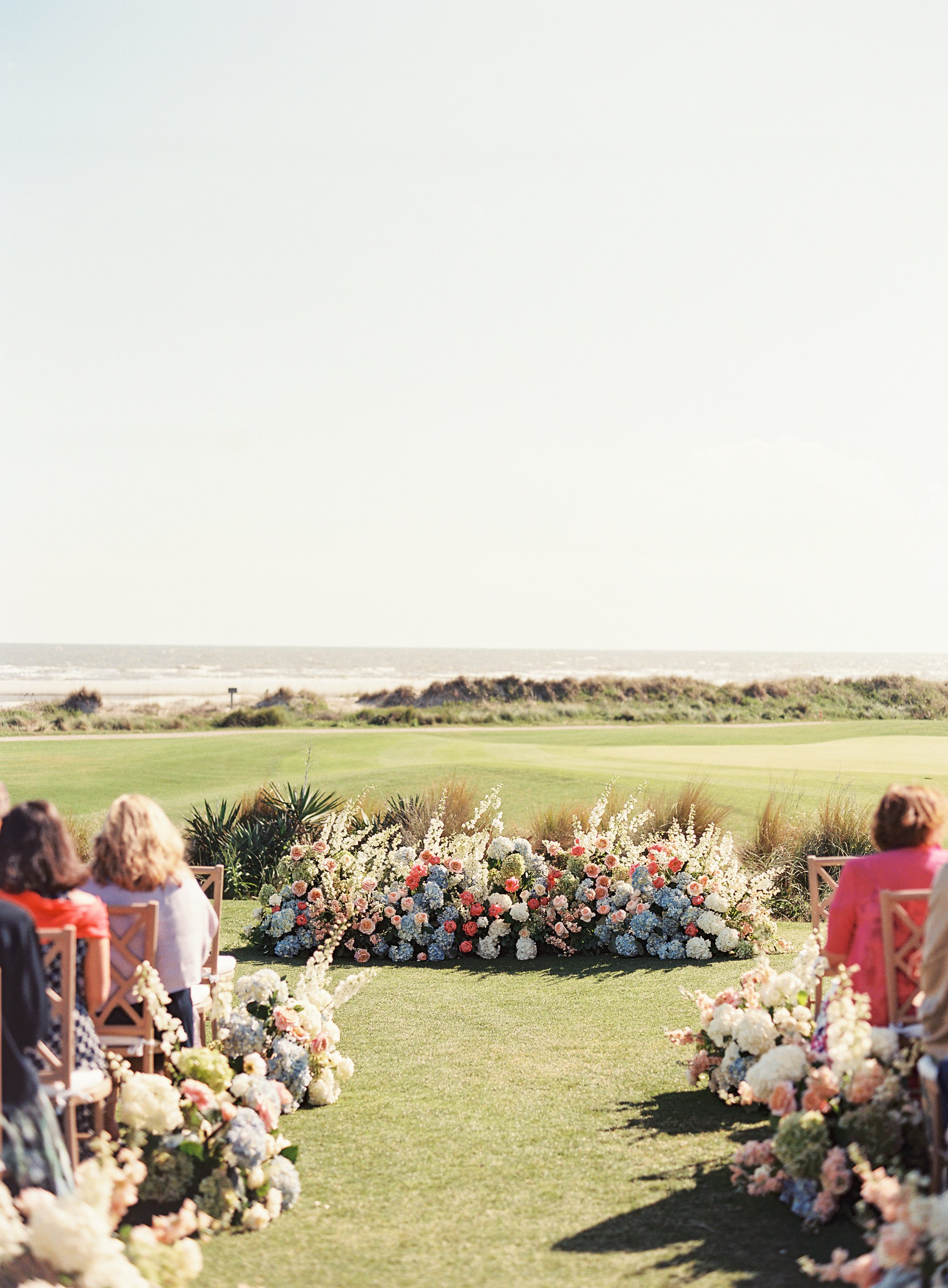 Outdoor wedding ceremony at the Ocean Course, Kiawah Island, South Carolina, with chairs and floral arrangements on a lush green lawn facing the ocean.