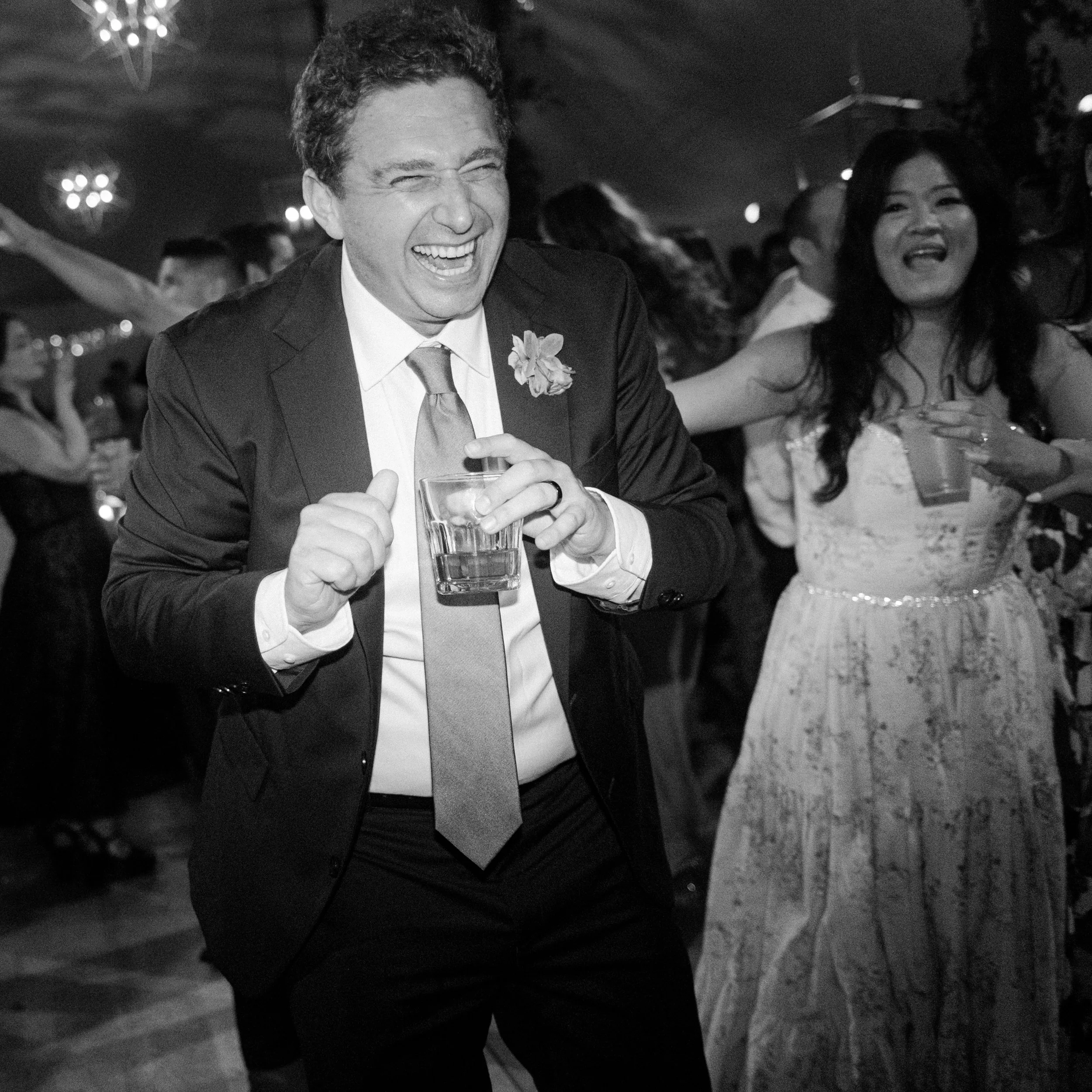 People enjoying a celebration, smiling, dancing, and holding drinks in a festive event.