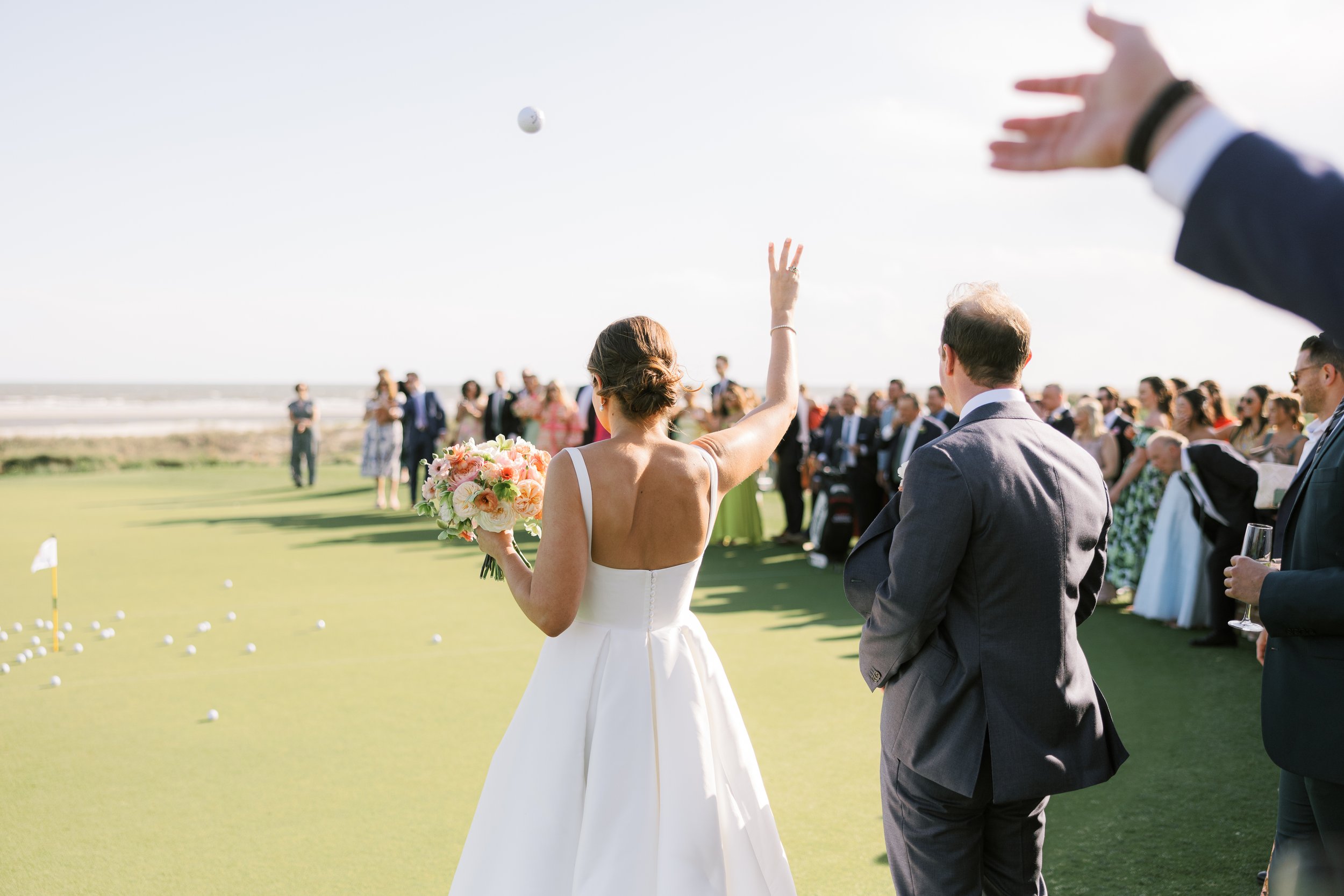 A woman in a white wedding dress throwing a golf ball into a golf hole on a sunny day at a wedding reception on the beach.