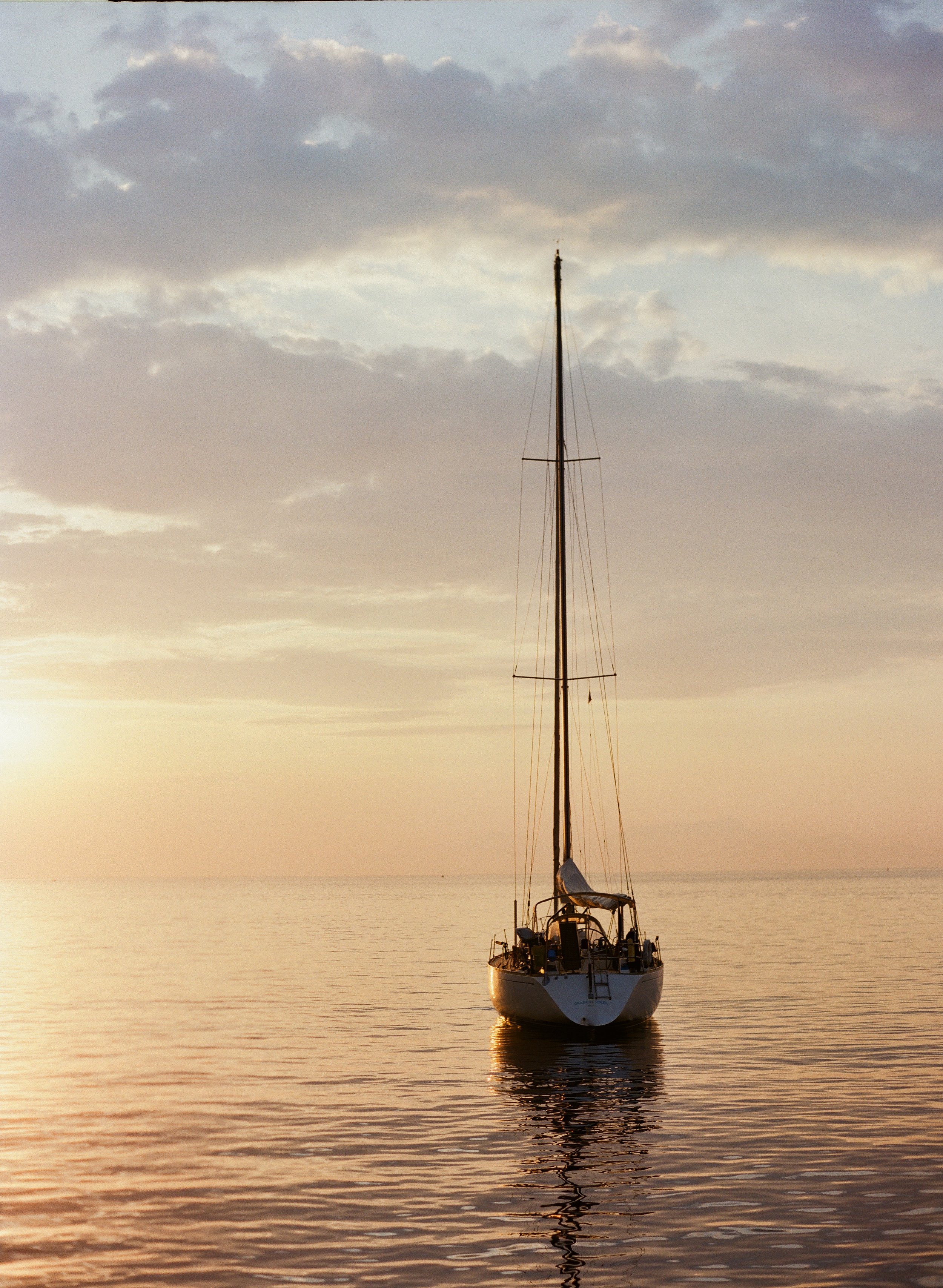 A sailboat floating on calm water in Positano, Italy, during sunset with a partly cloudy sky.