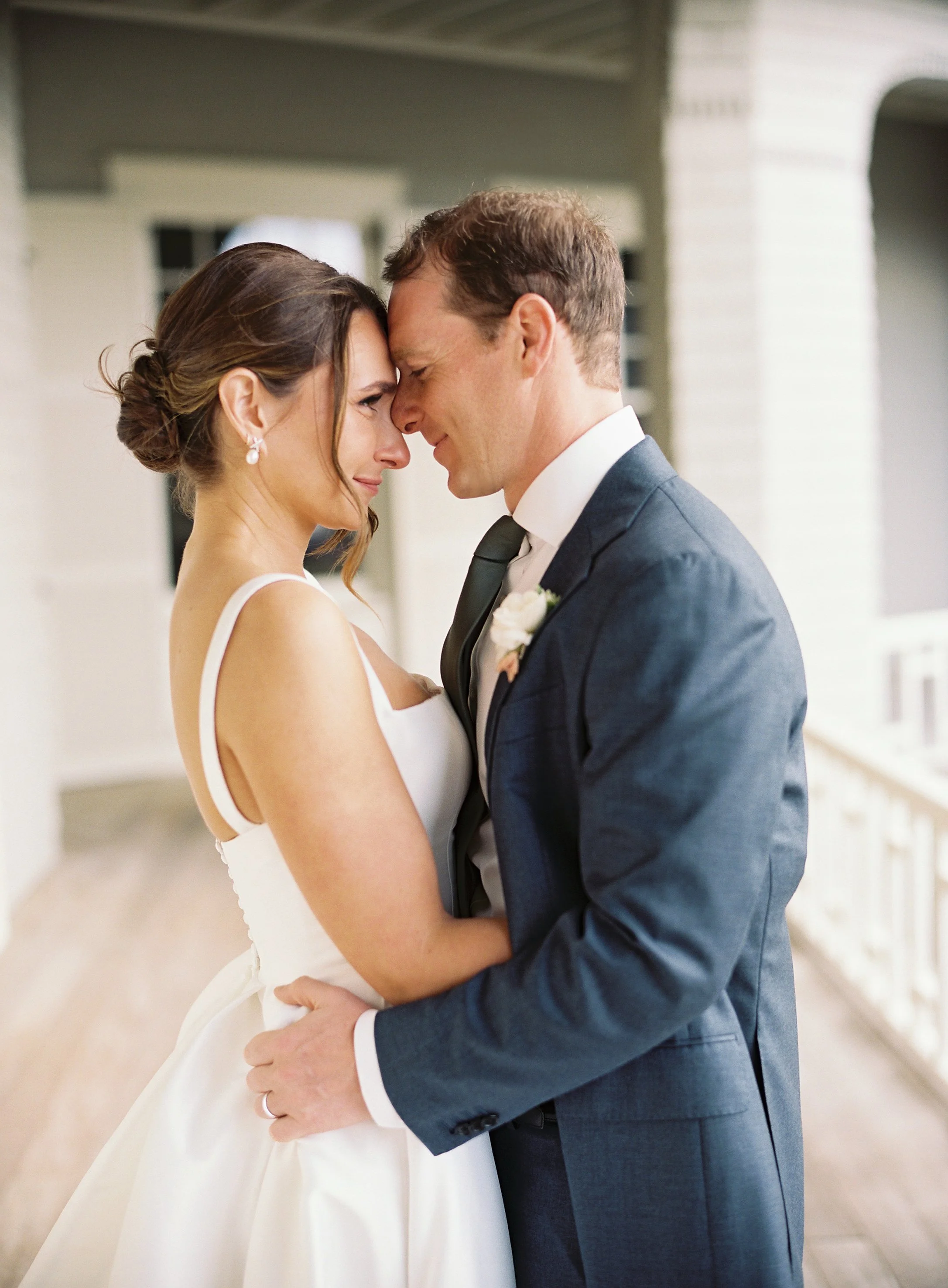 A bride and groom with foreheads touching, eyes closed, embracing in a tender moment during their wedding.