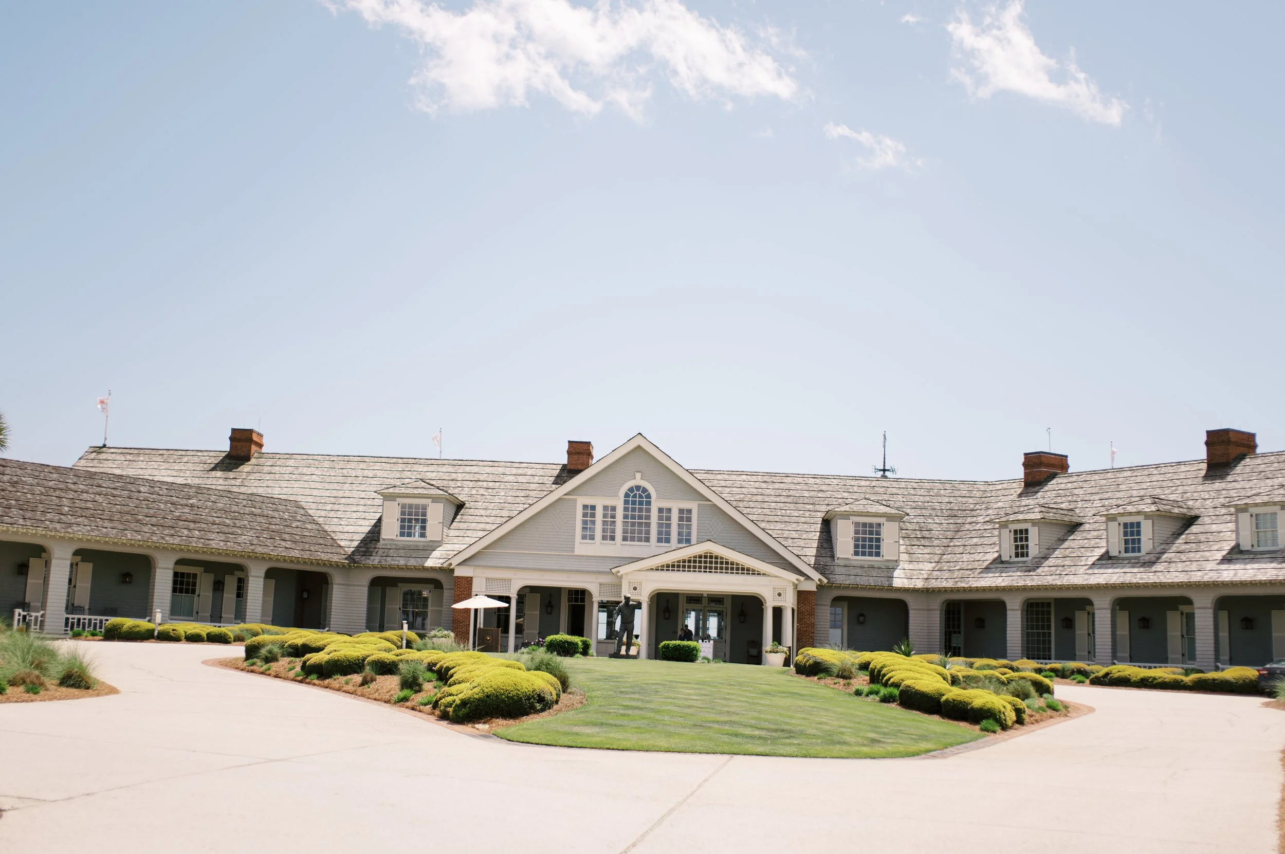 Large white house with a landscaped front yard, lawn, and walkways, under a blue sky.