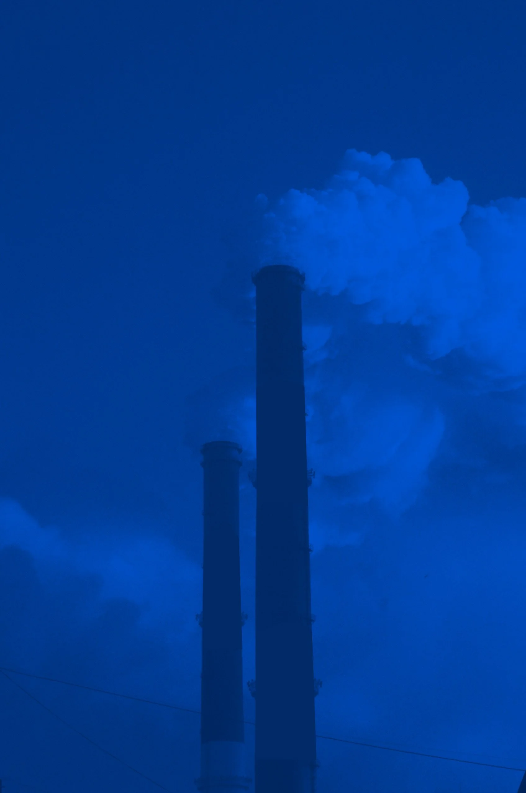 Two industrial smokestacks emitting smoke under blue-toned lighting.