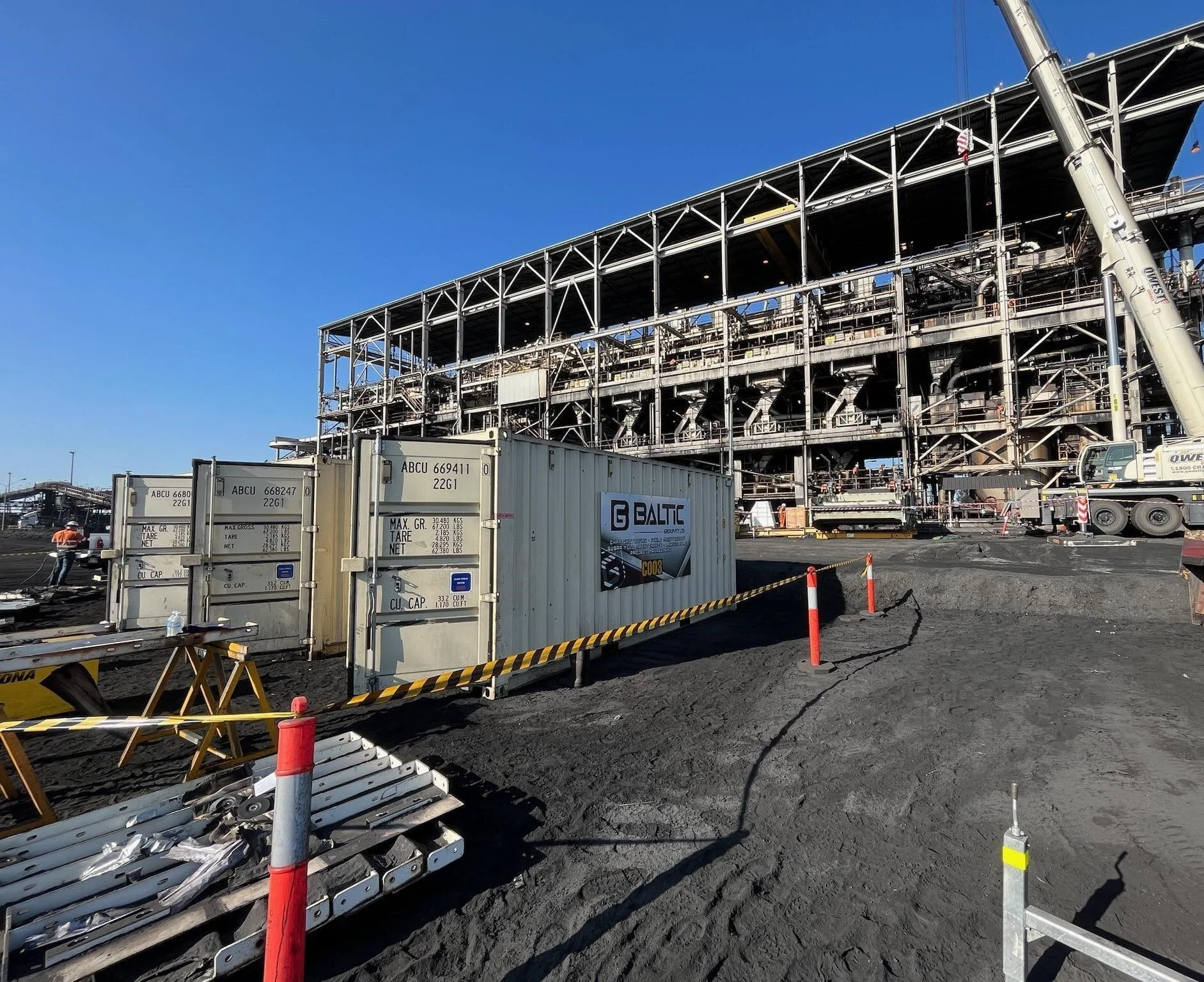 Construction site with industrial building framework, shipping containers, and construction equipment.