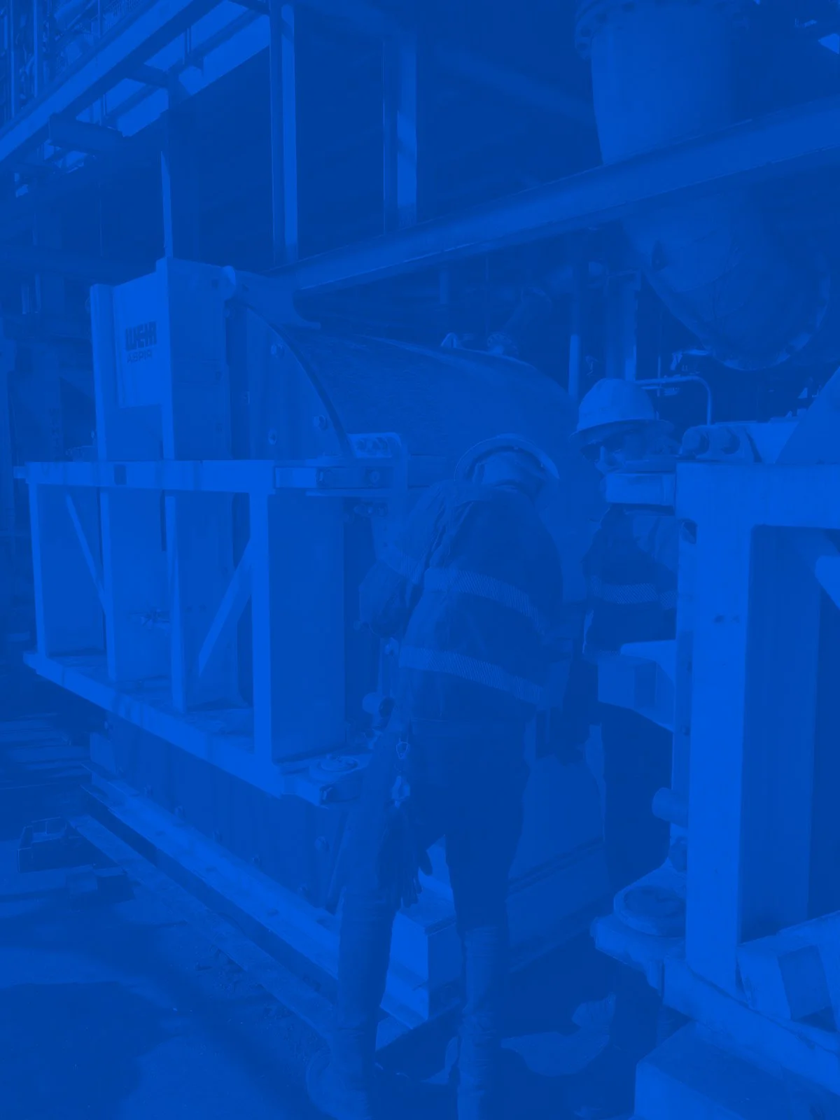 Industrial workers with machinery in a factory setting under blue-colored filter.
